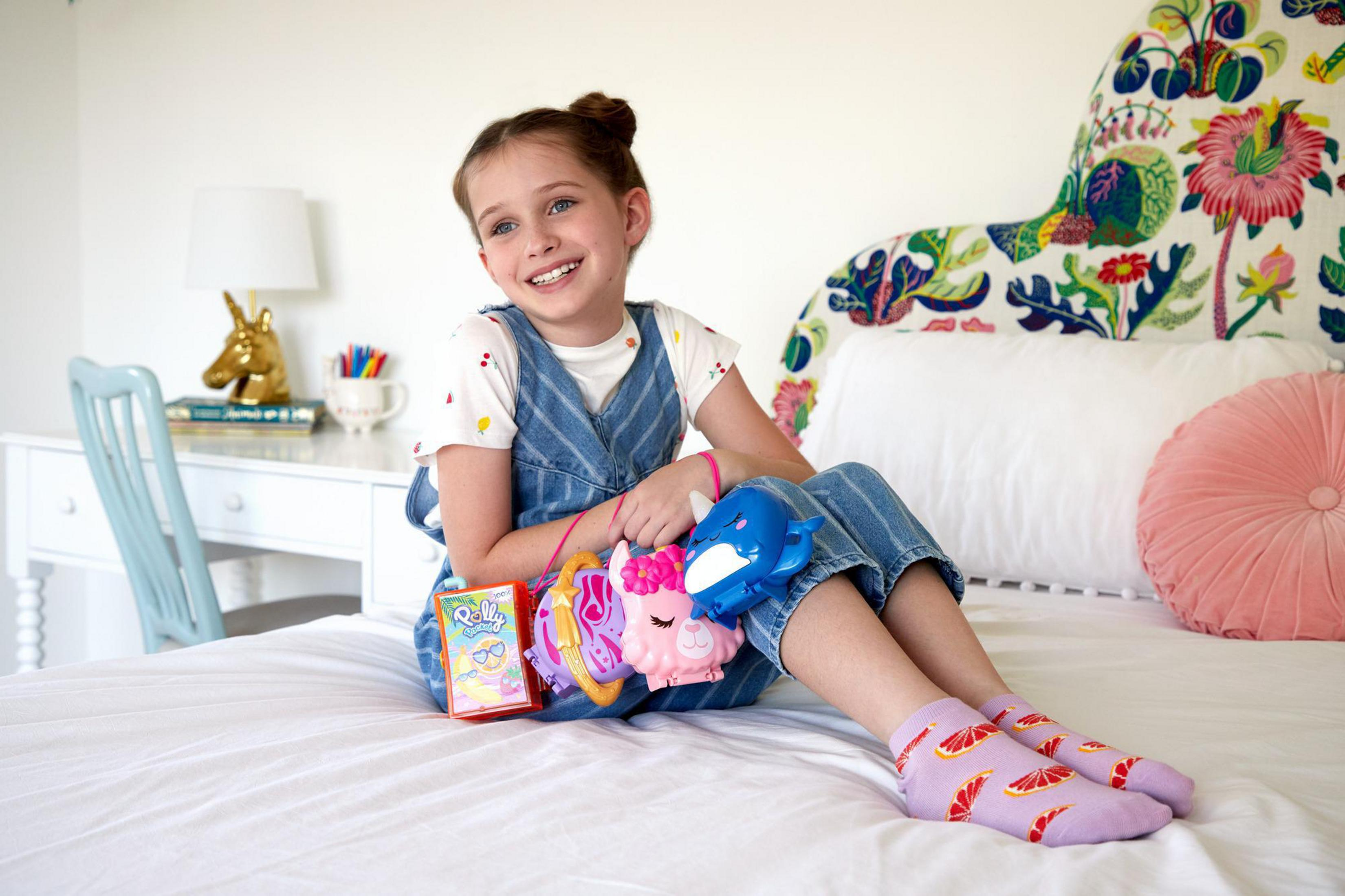 Niña sonriendo con juguetes. Sentada en la cama, sosteniendo juguetes, sonriendo y con calcetines coloridos.