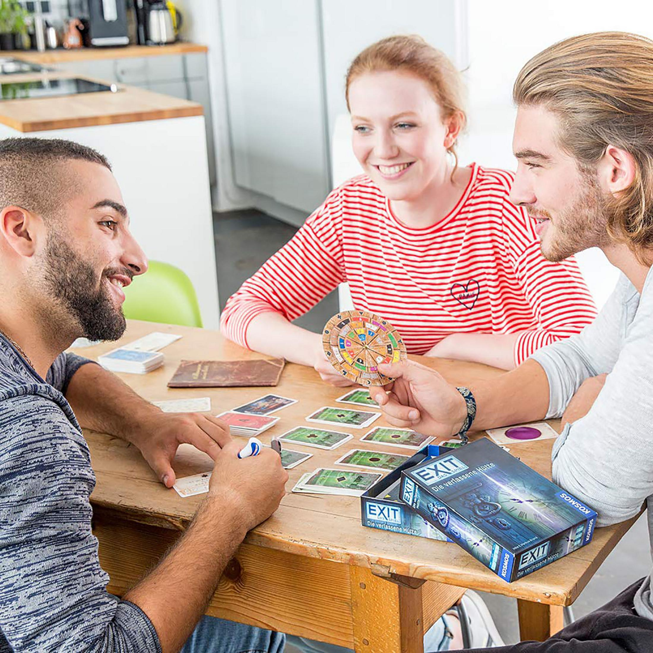 Drei Personen spielen ein Brettspiel. Einer hält ein Spielteil.