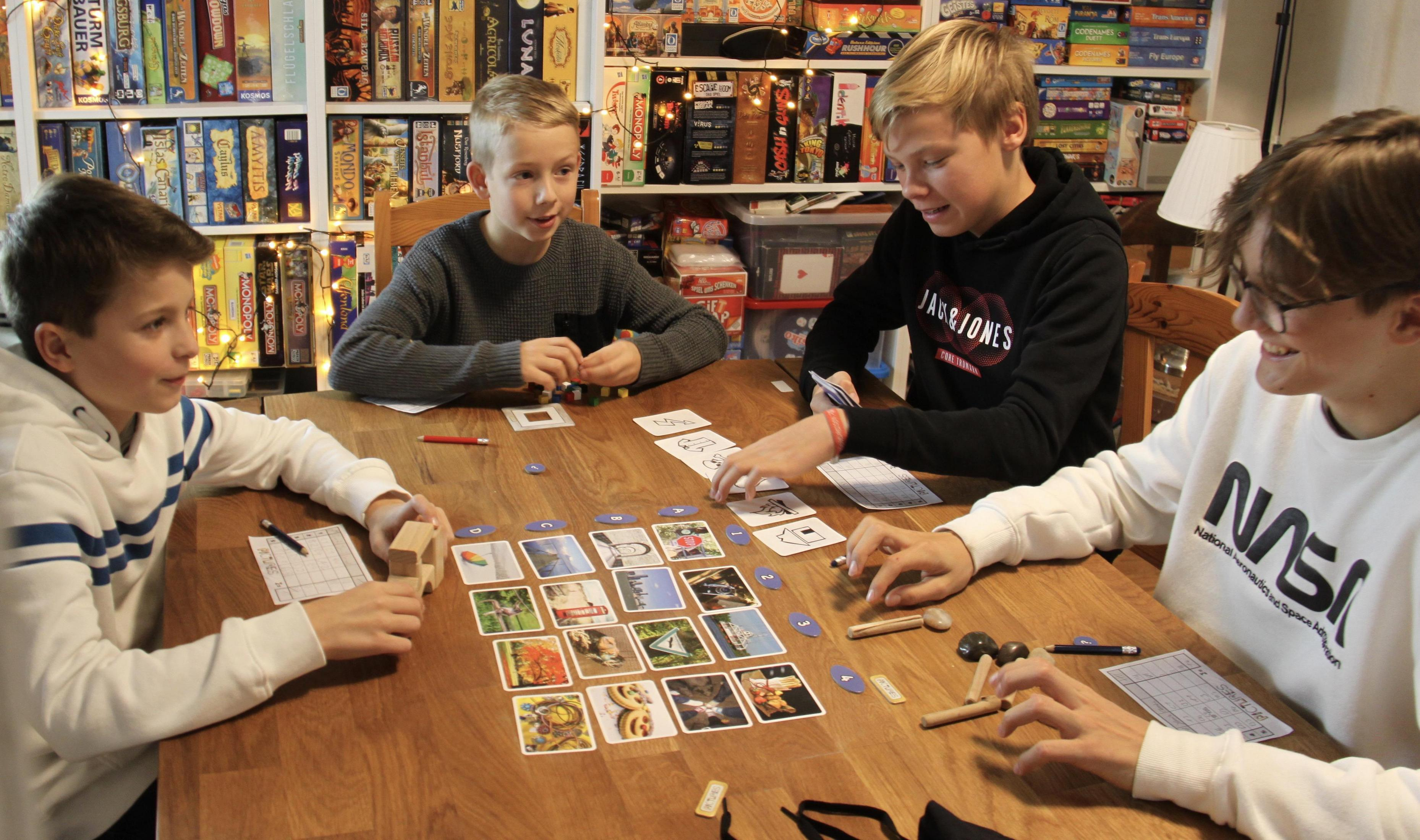 Vier Personen spielen ein Brettspiel an einem Tisch. Verschiedene Karten und Spielsteine sind ausgebreitet.