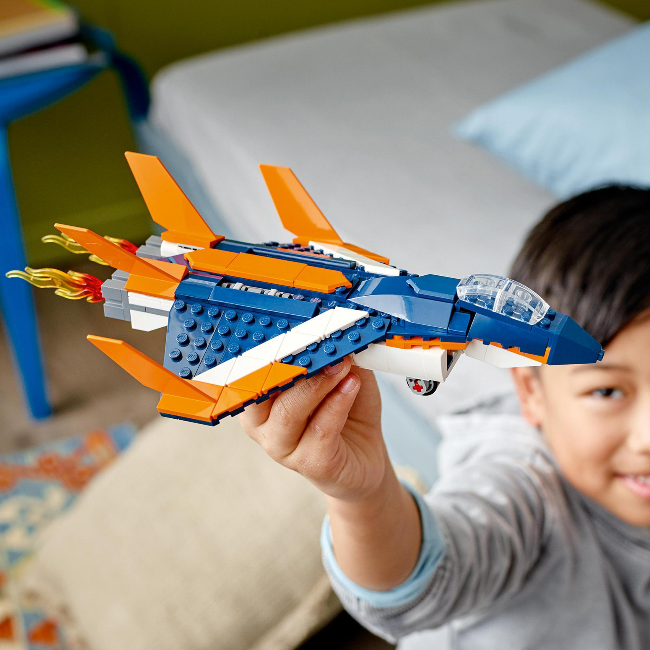 Un niño sostiene un avión de juguete azul y naranja. El avión tiene alas y llamas.