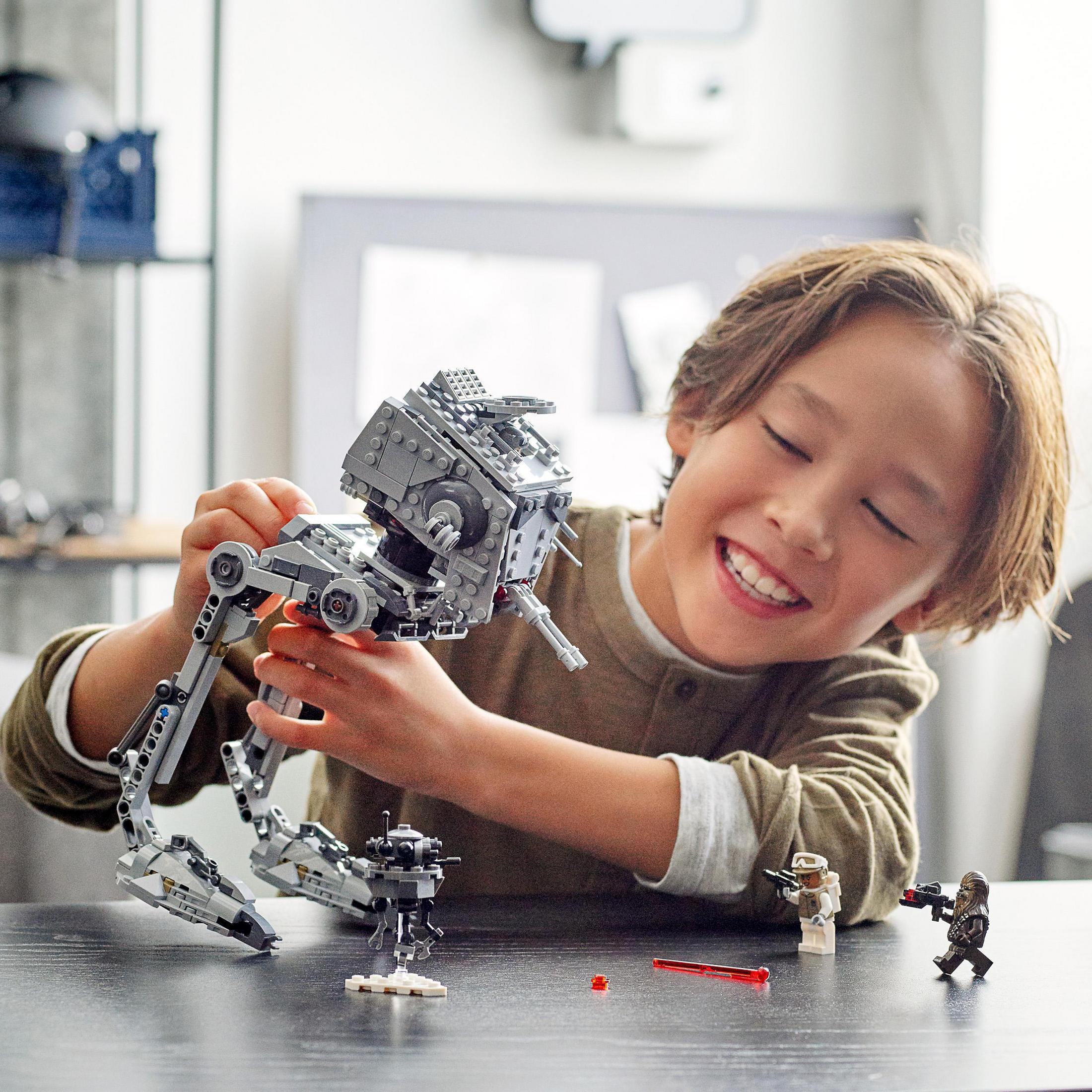 Ein Junge spielt mit einem Star Wars AT-ST Lego-Set.  Andere Lego-Figuren und Sets sind ebenfalls vorhanden.