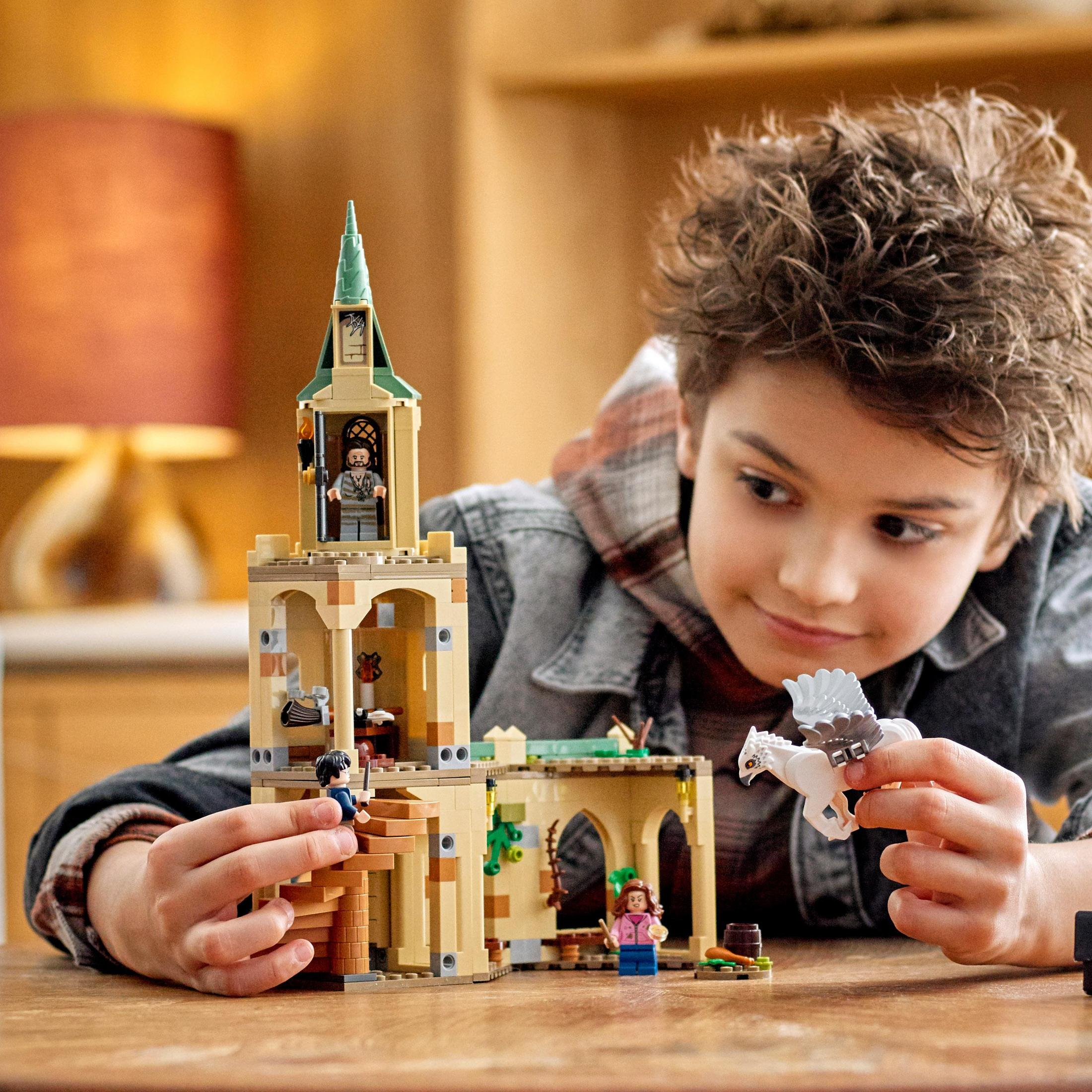 Een jongen speelt met een Lego-set. Een toren en beeldjes zijn zichtbaar. De jongen glimlacht.