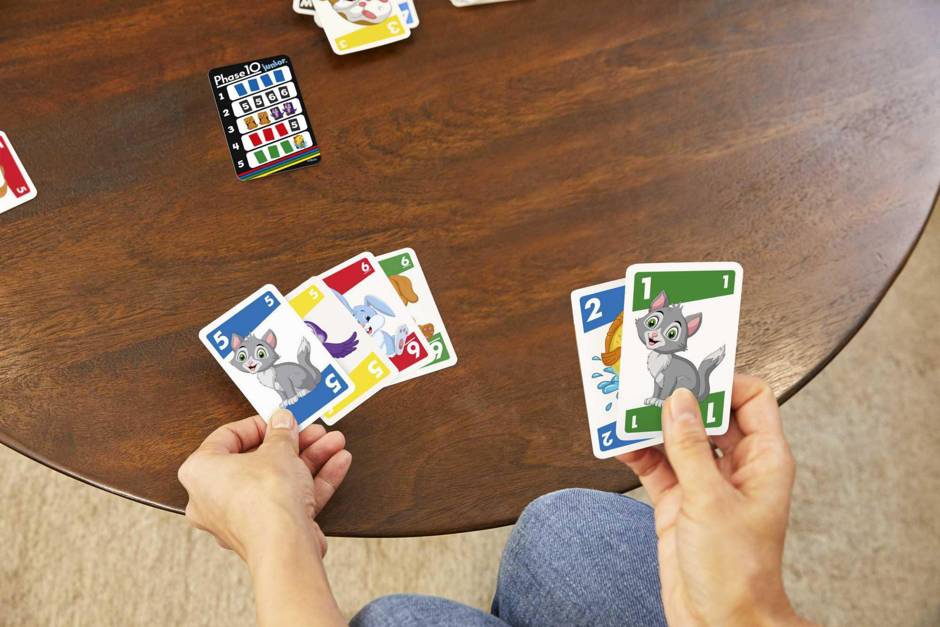 Mani che tengono carte del gioco di carte Phase 10 su un tavolo di legno.