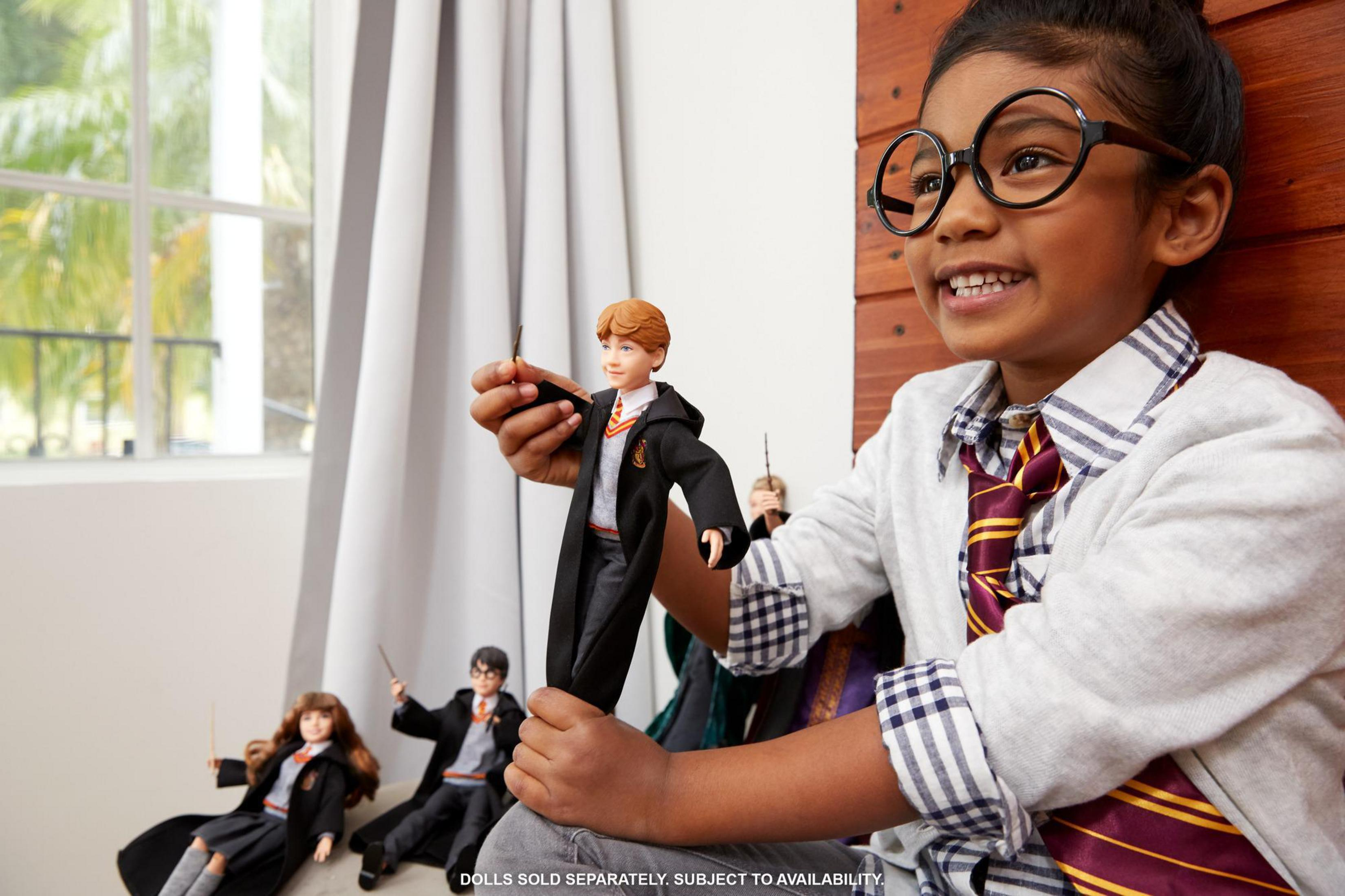 Ein junges Mädchen mit Brille hält eine Puppe von Ron Weasley und andere Harry Potter Puppen.