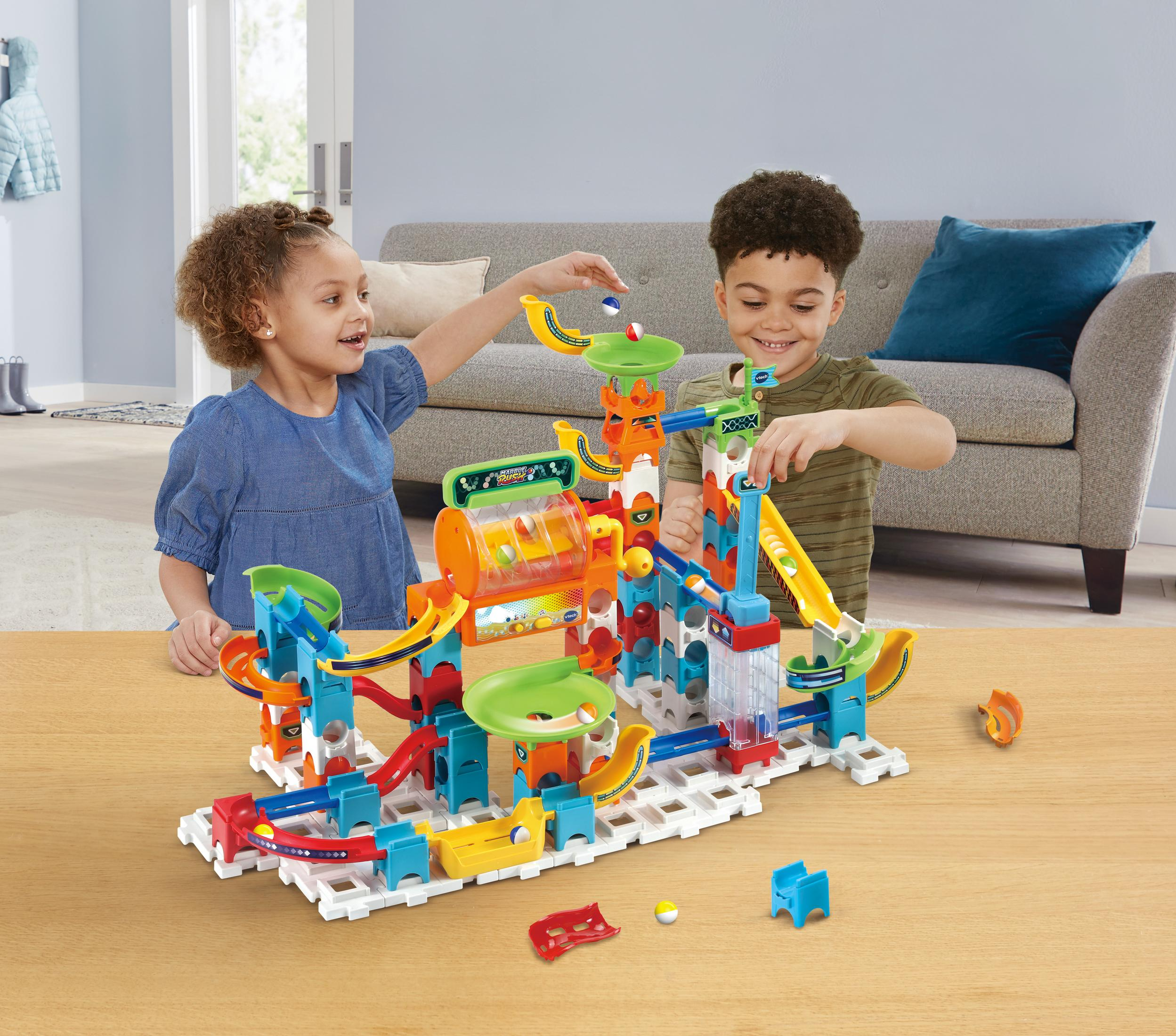Zwei Kinder spielen mit einem komplexen Murmelbahn-Spielzeug auf einem Holztisch.