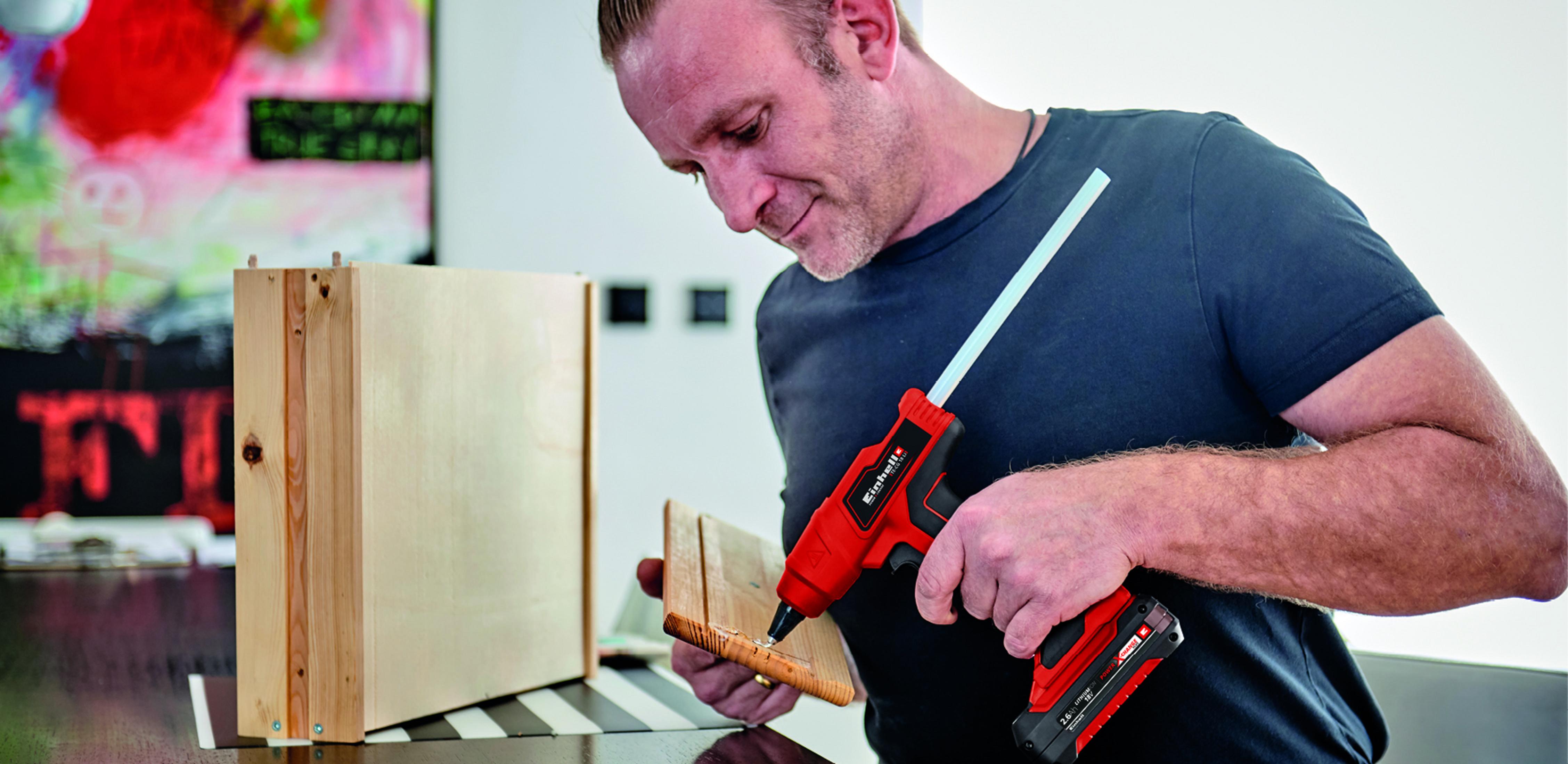 Mężczyzna używa czerwonego pistoletu do klejenia, aby przymocować drewno.