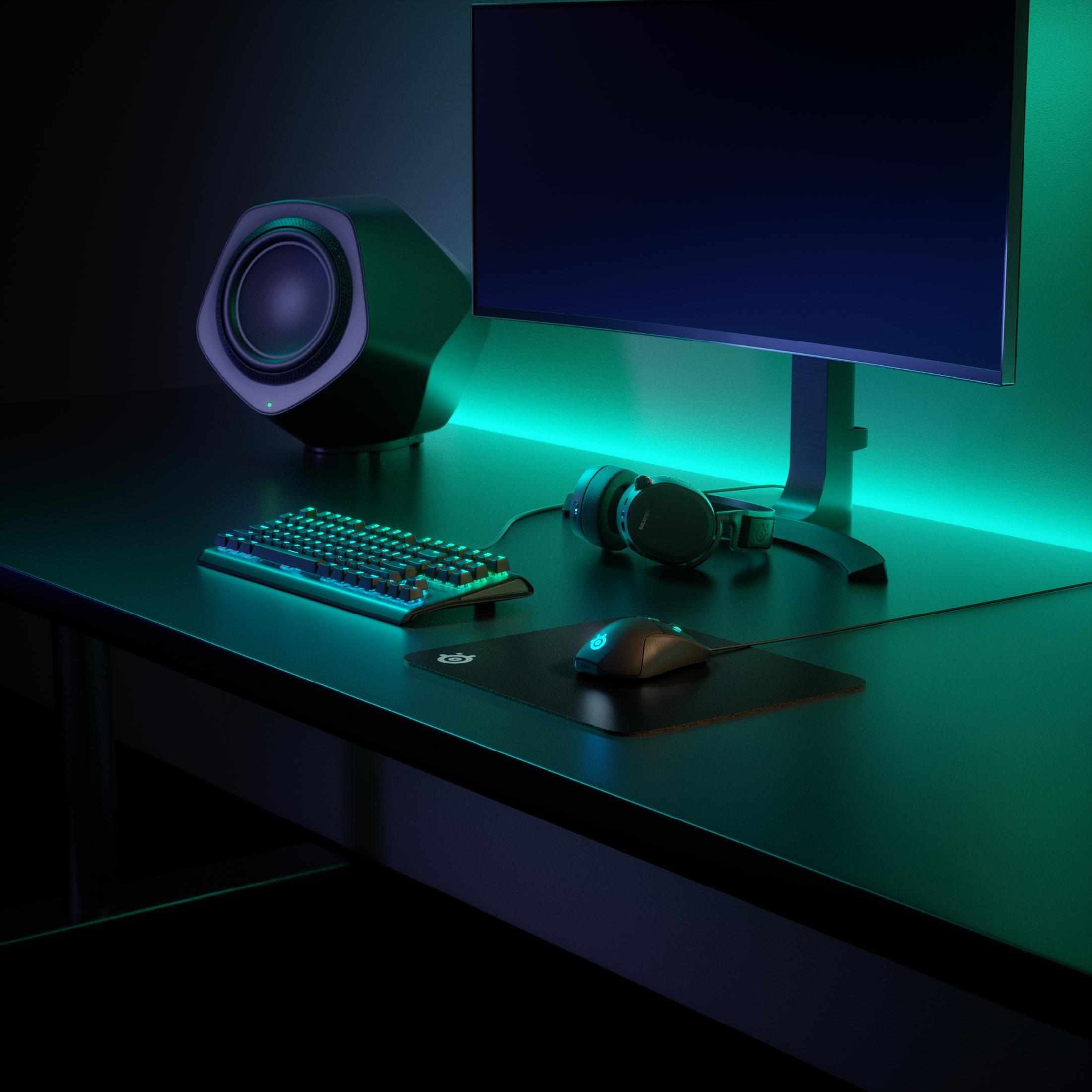 Configuración de juegos con monitor, teclado, ratón, auriculares y altavoz, todo en un escritorio negro.