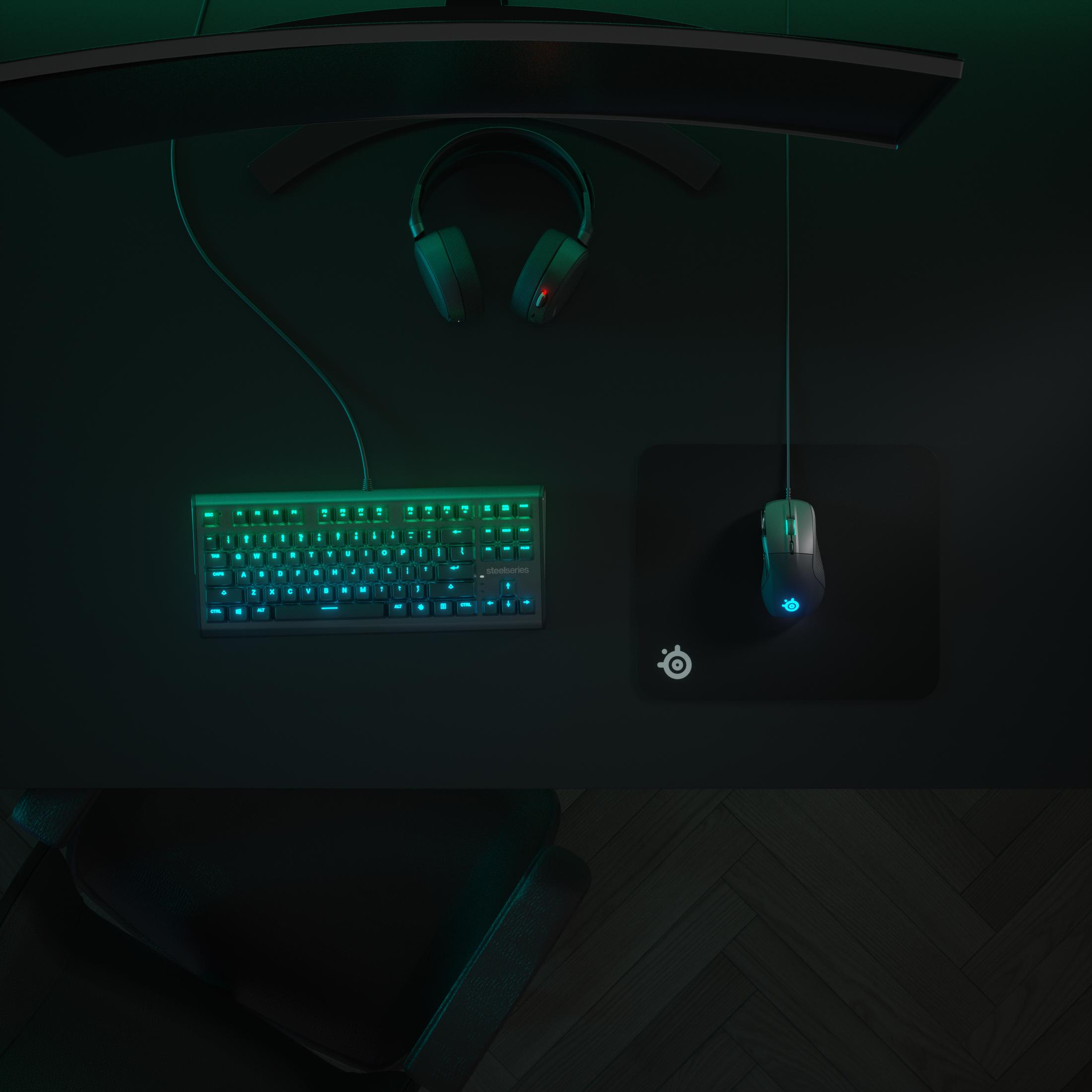 Vista superior de un escritorio negro con teclado, ratón y auriculares. La configuración tiene iluminación verde y azul.