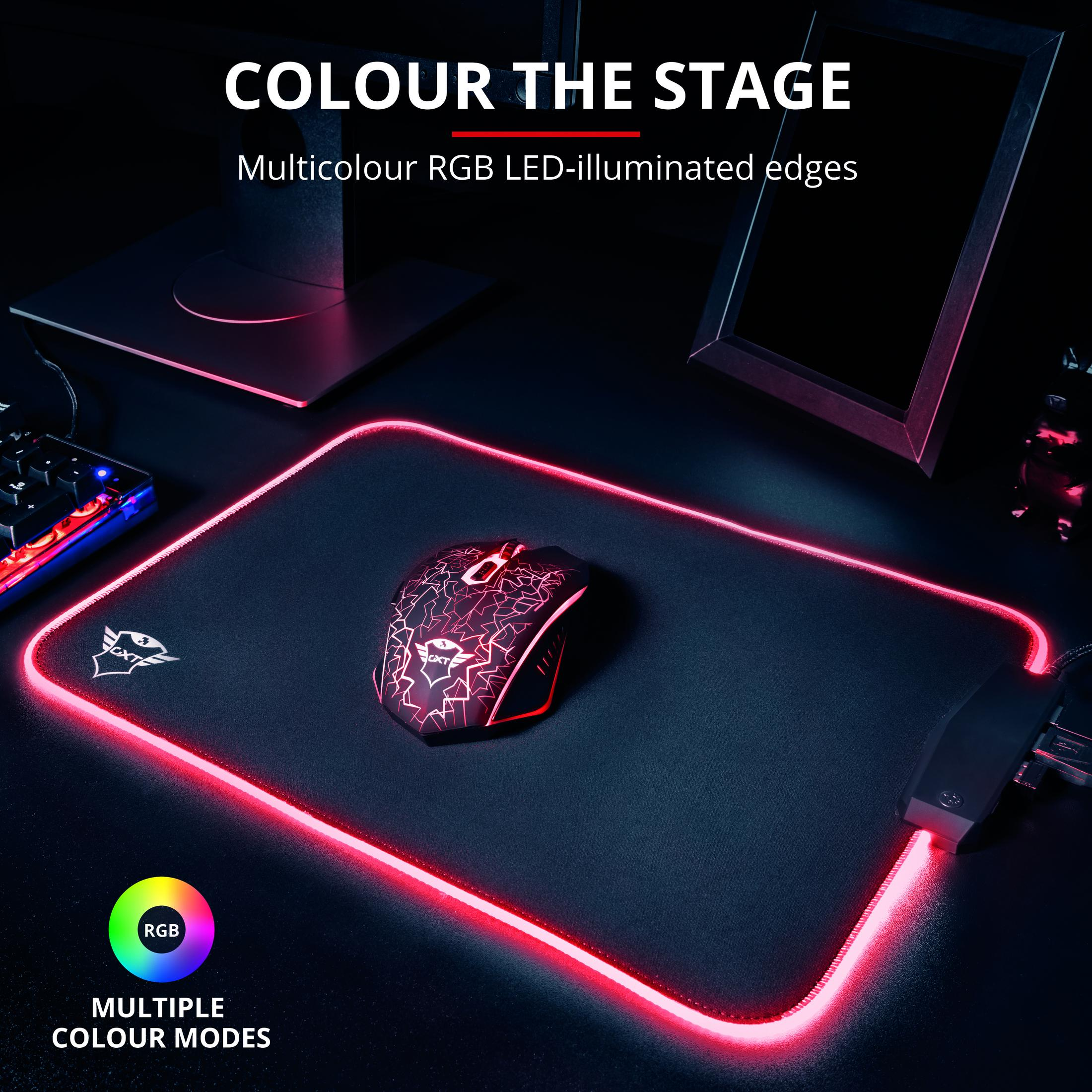 Czarna mysz na czarnej podkładce z podświetleniem RGB, klawiatura i monitor w tle.