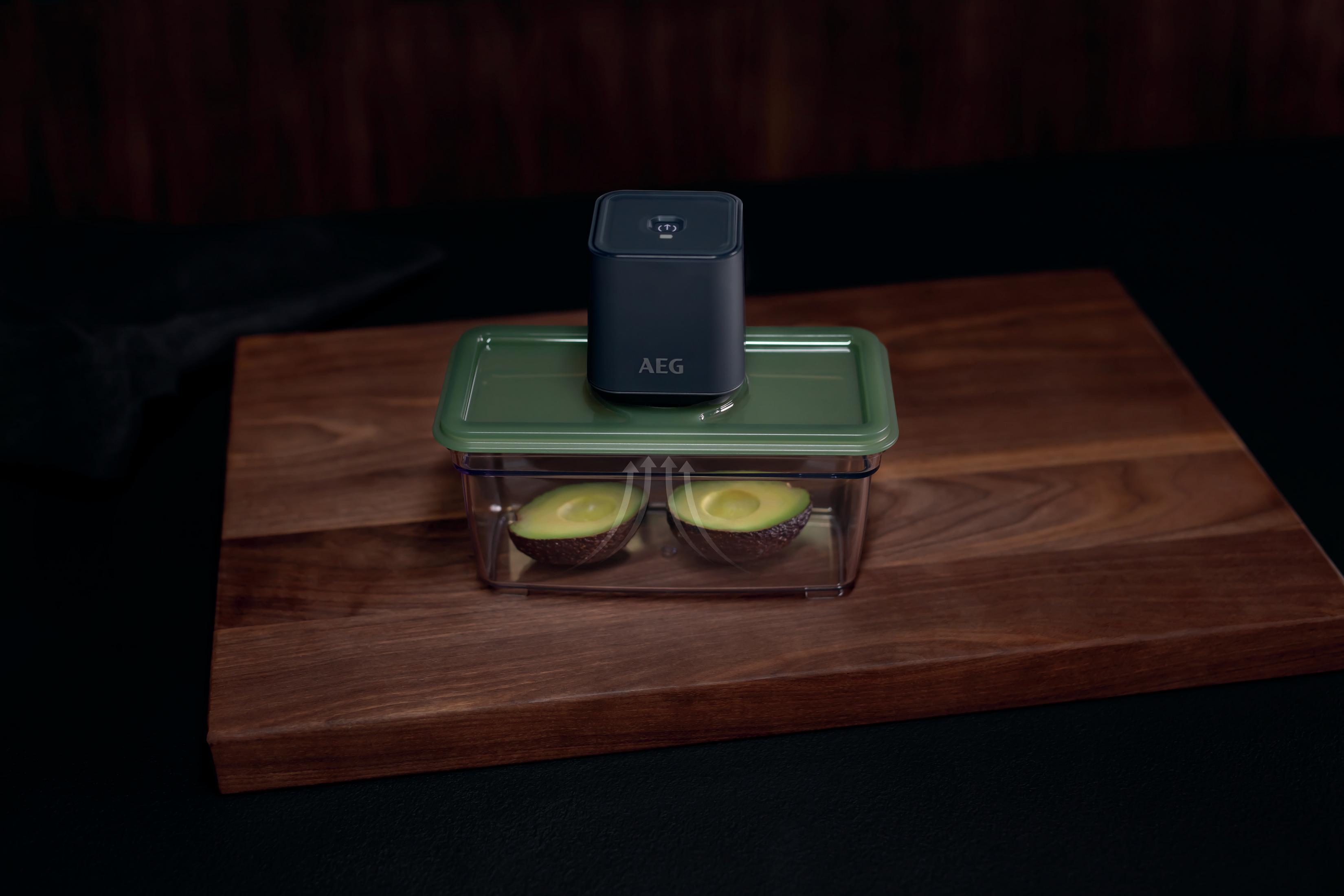 Mitades de aguacate en un recipiente transparente, selladas al vacío. Máquina AEG encima, en tabla de madera.