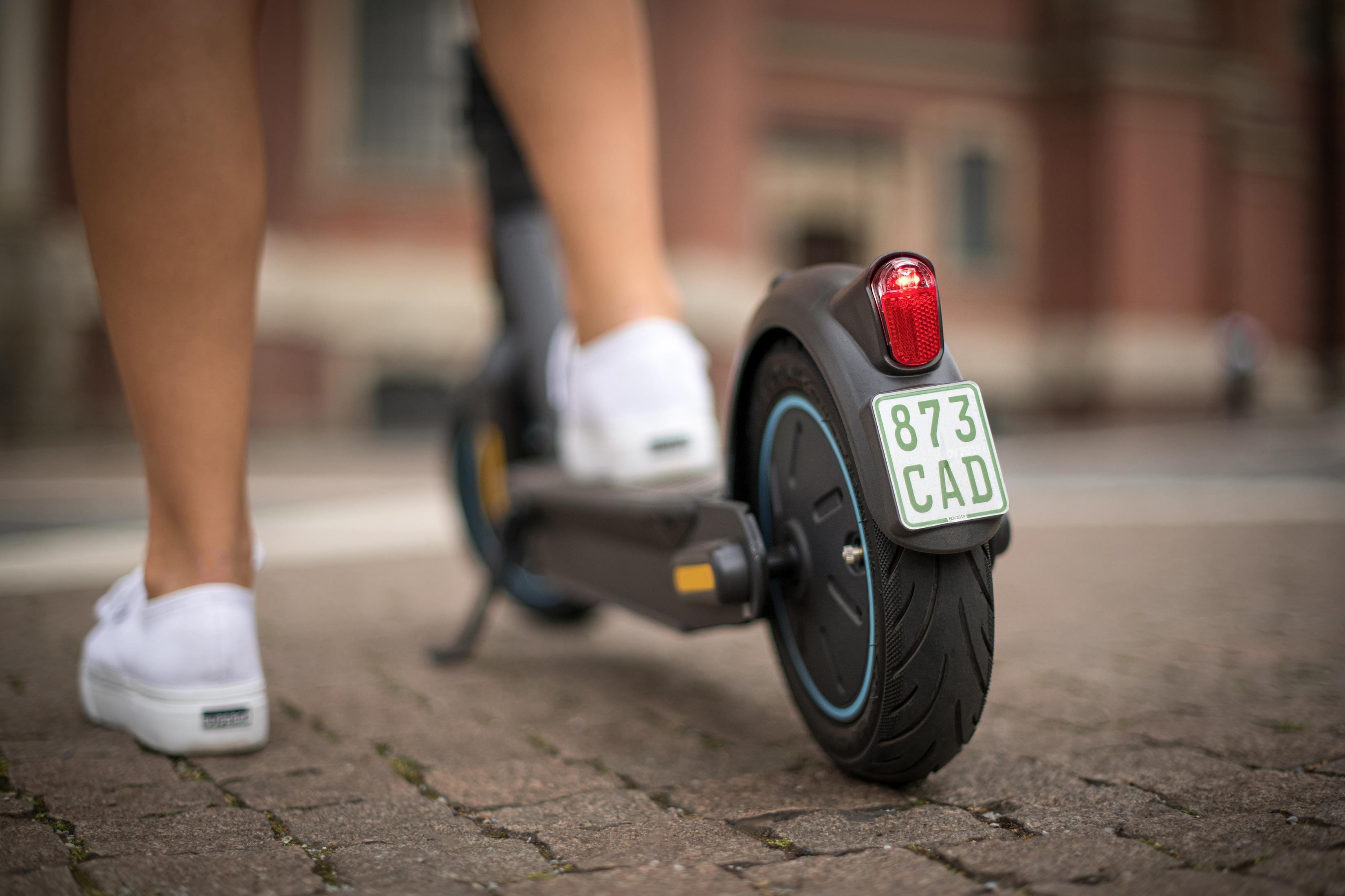 Person fährt einen Elektroroller, zeigt Hinterrad, Kennzeichen und Rücklicht.