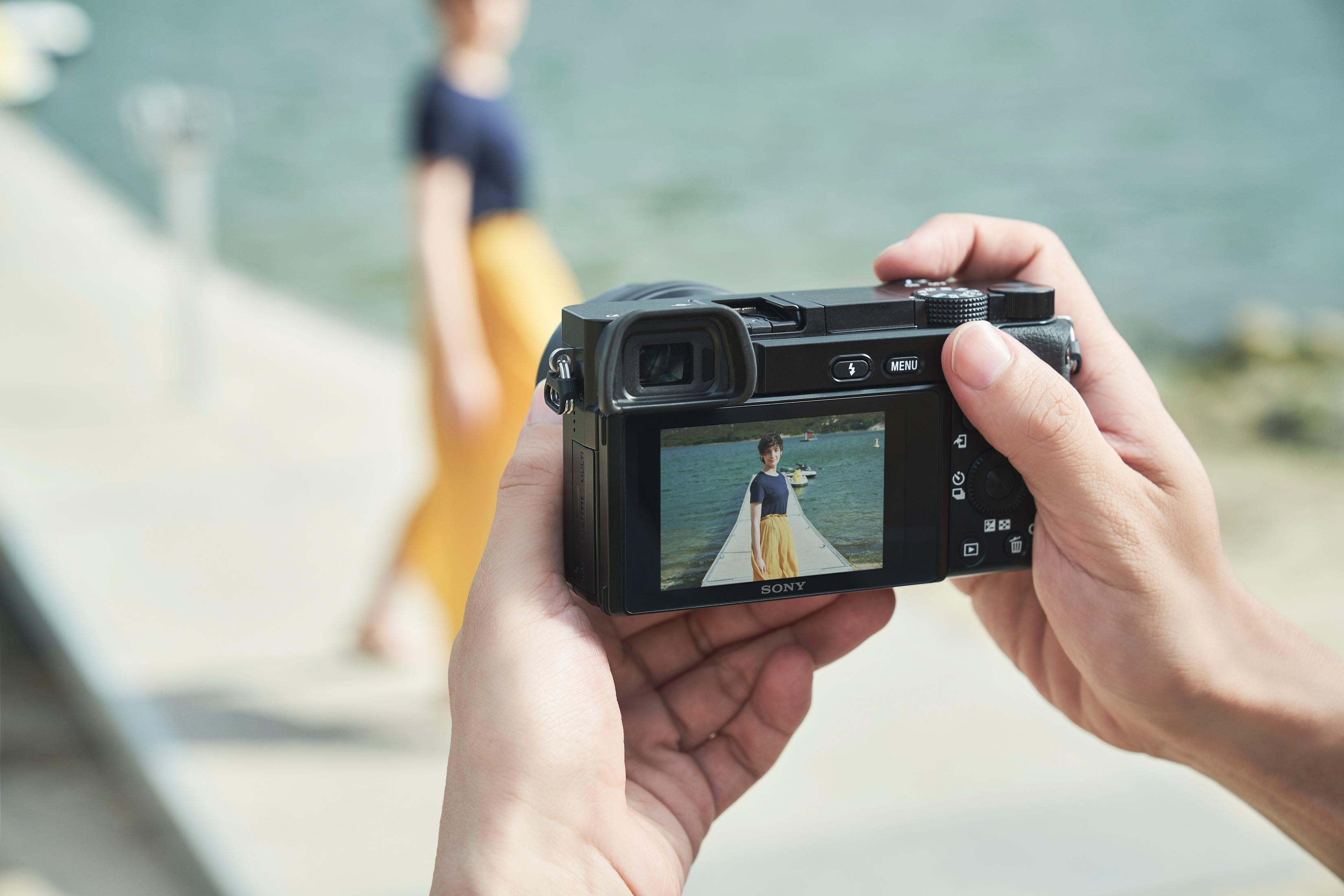 Person hält Kamera, macht Foto von Frau auf Holzsteg.