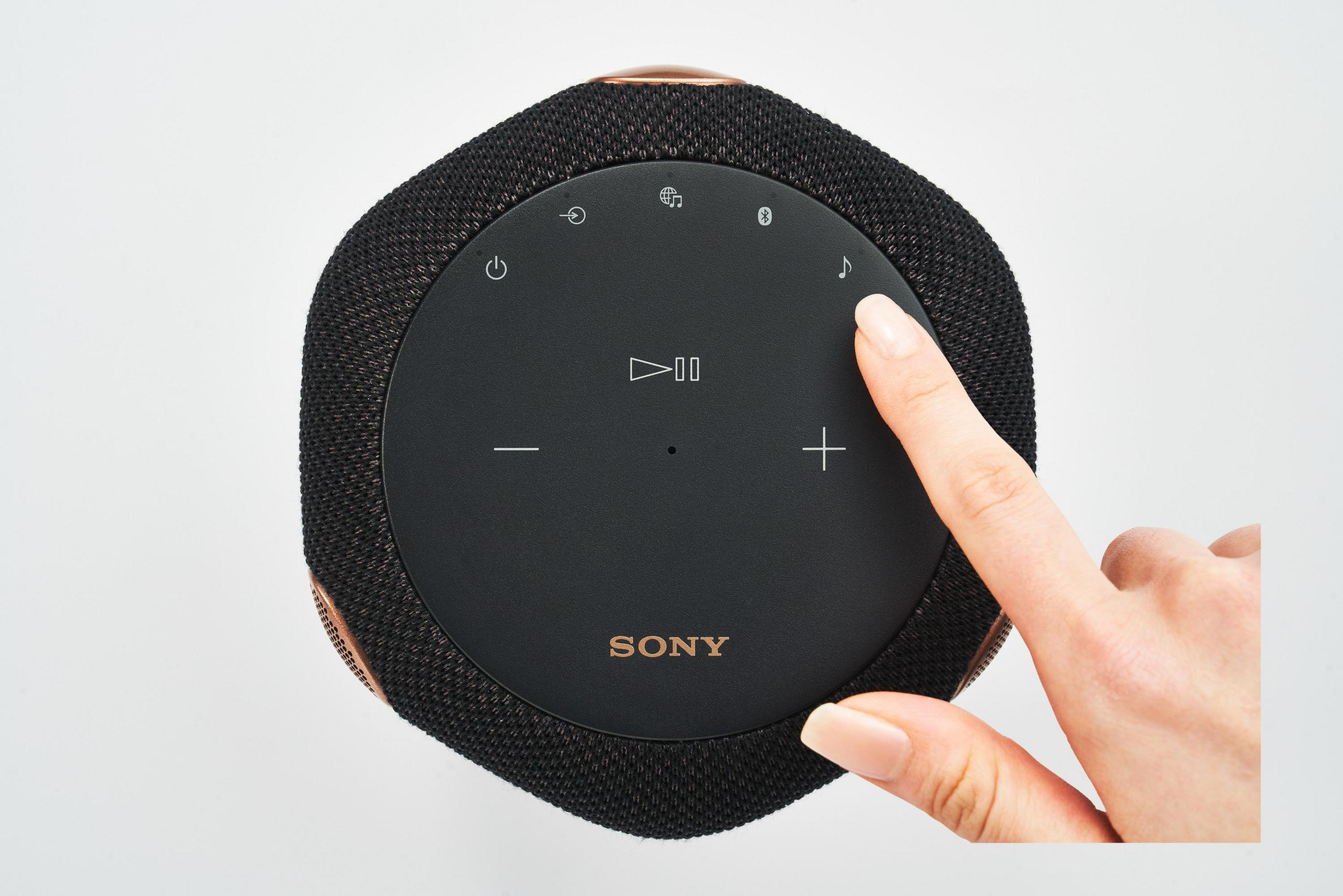Schwarzer Lautsprecher mit Touch-Bedienelementen und einem Finger, der das Musiknoten-Symbol berührt.