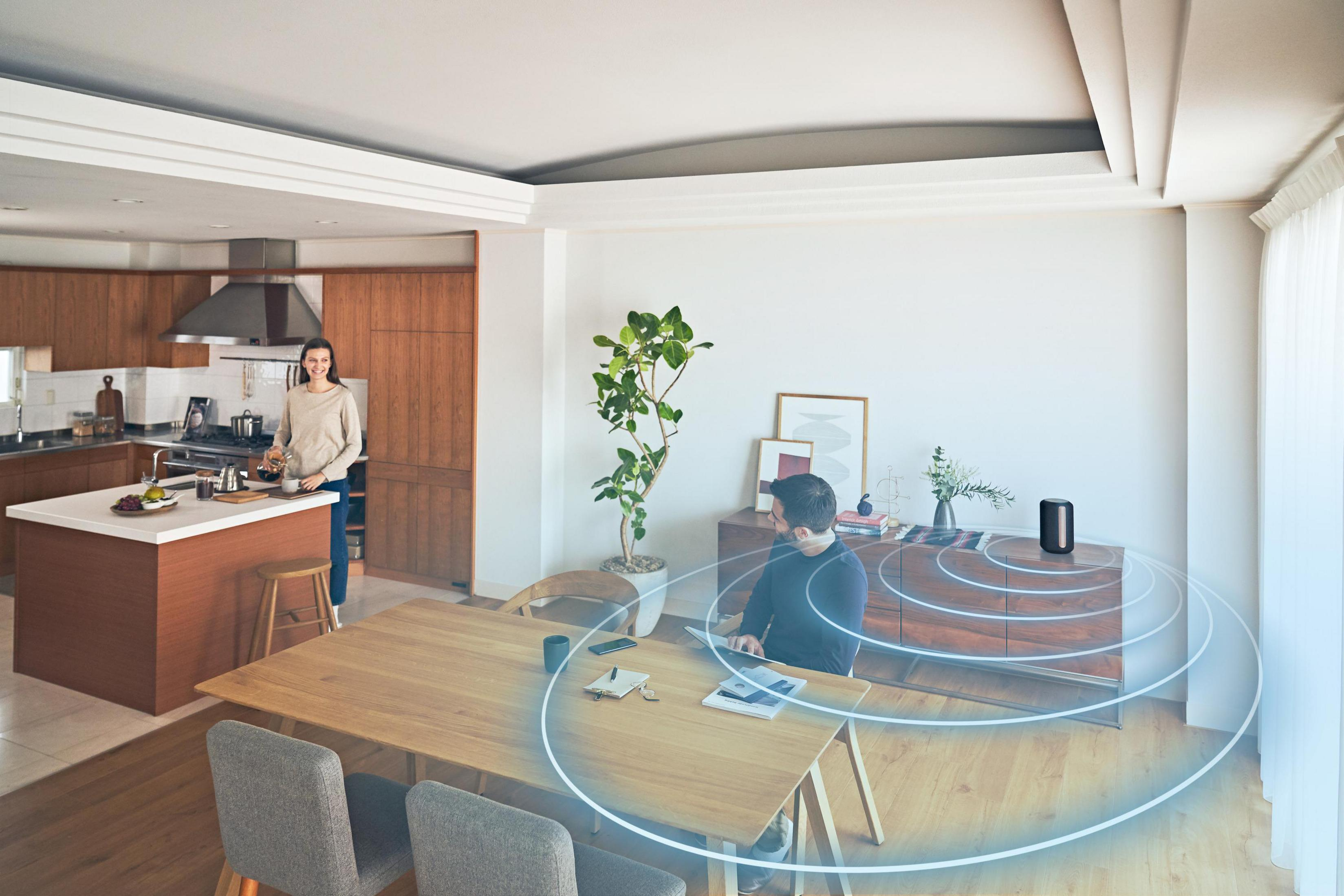 Wohnzimmer mit Personen, einem Lautsprecher und Schallwellengrafiken.