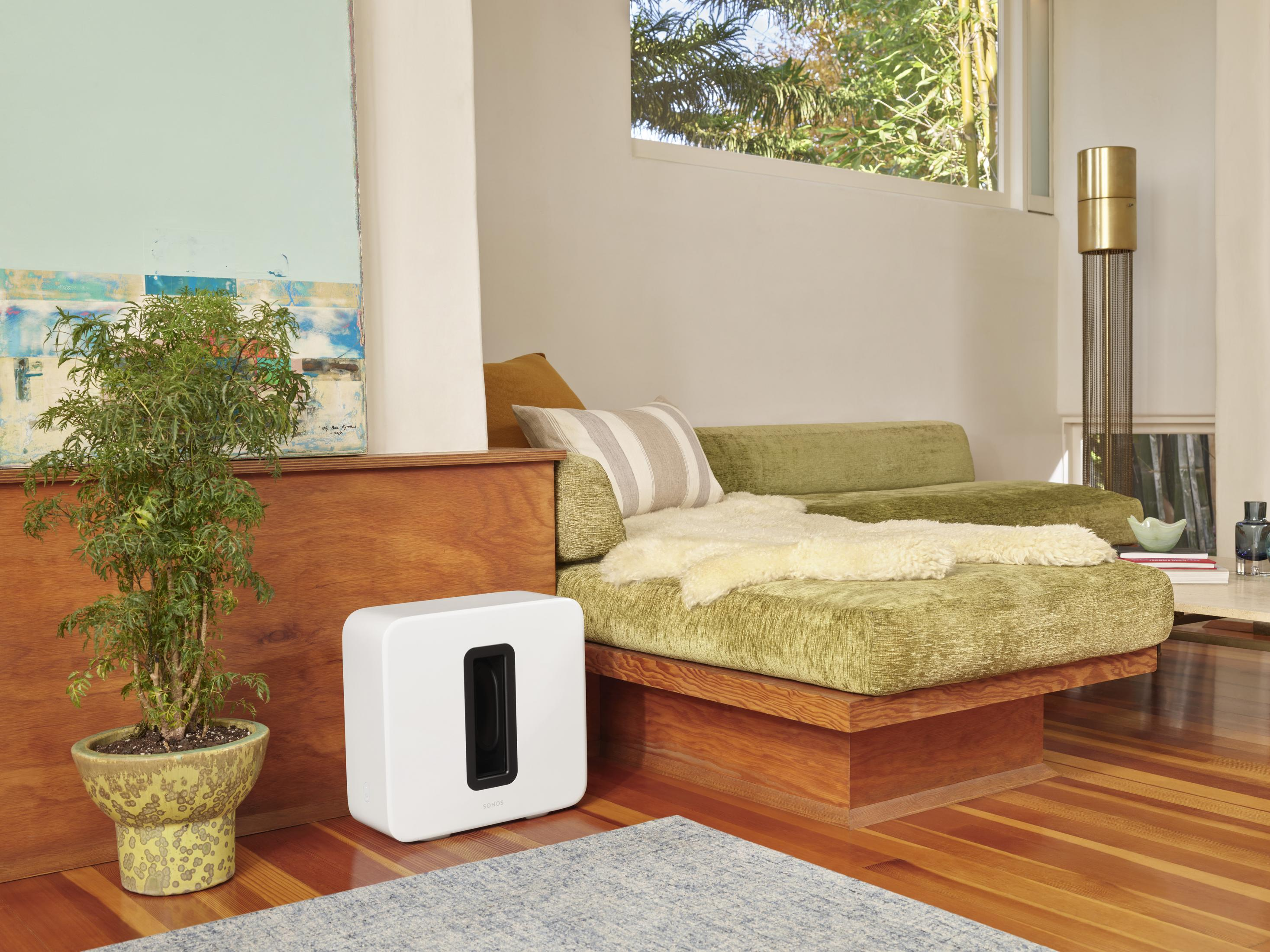 Subwoofer bianco accanto a un divano verde con una struttura in legno e una pianta.