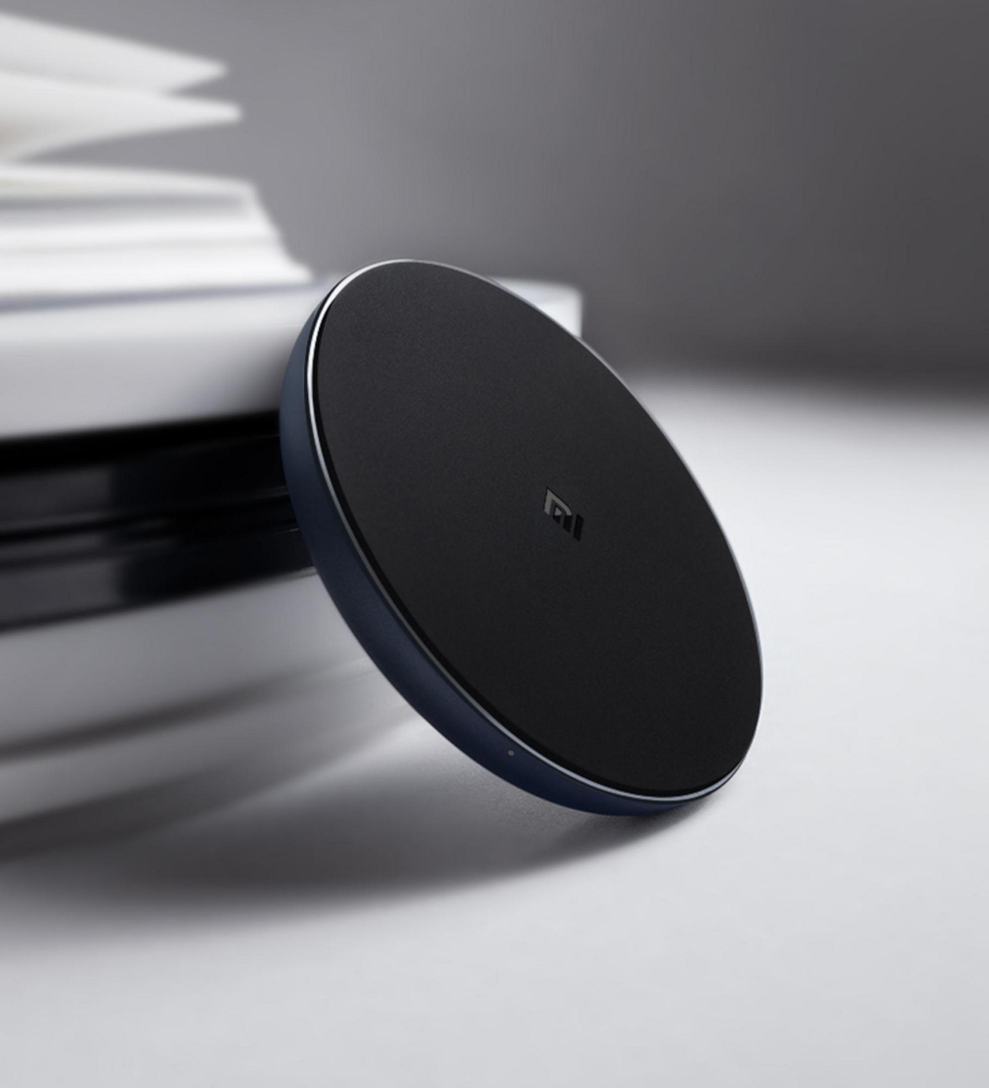 Czarna bezprzewodowa podkładka ładująca. Leży na białej powierzchni obok stosu książek. Marka to Mi.