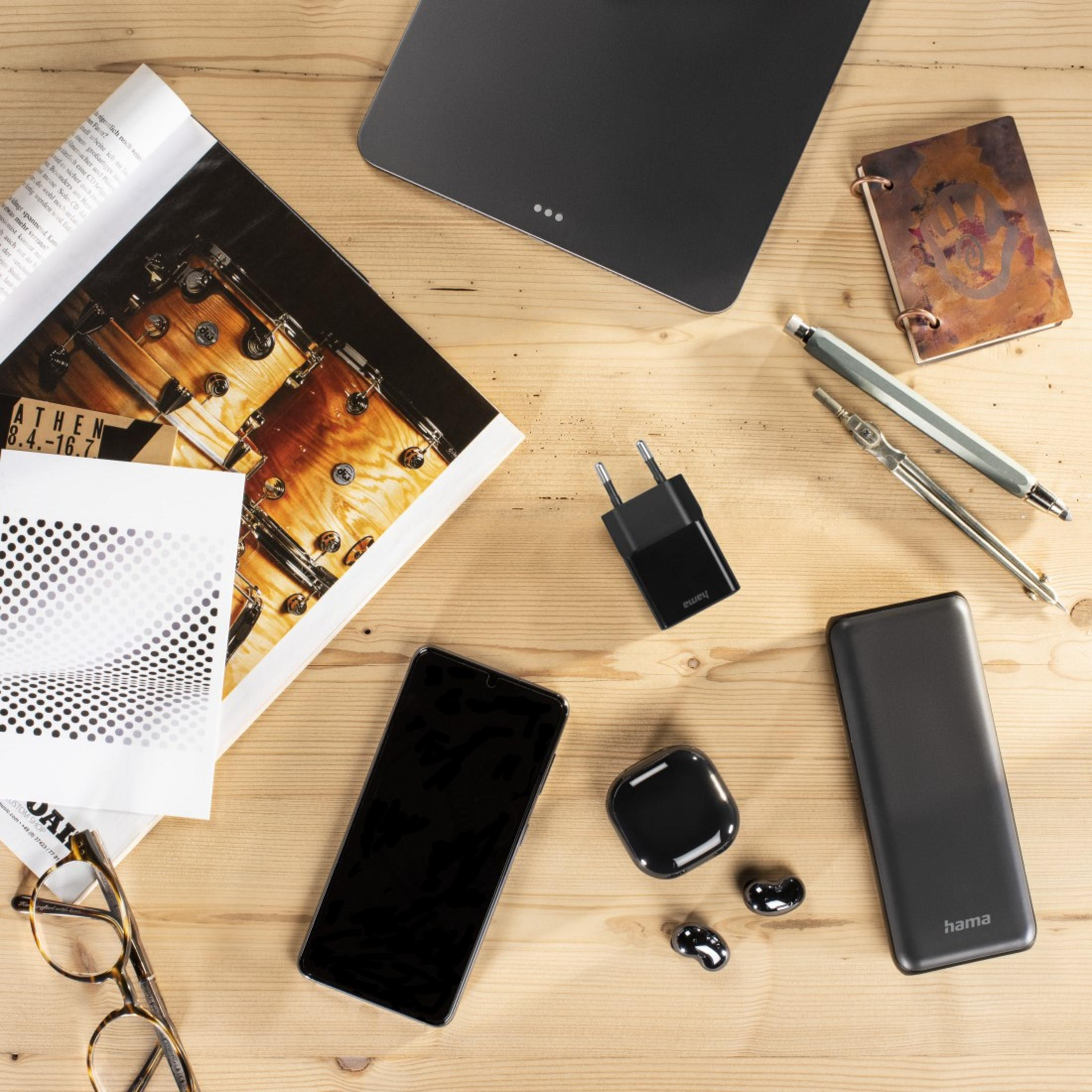 Drewniany stół zawiera tablet, telefon, słuchawki, ładowarkę, długopisy i czasopisma.