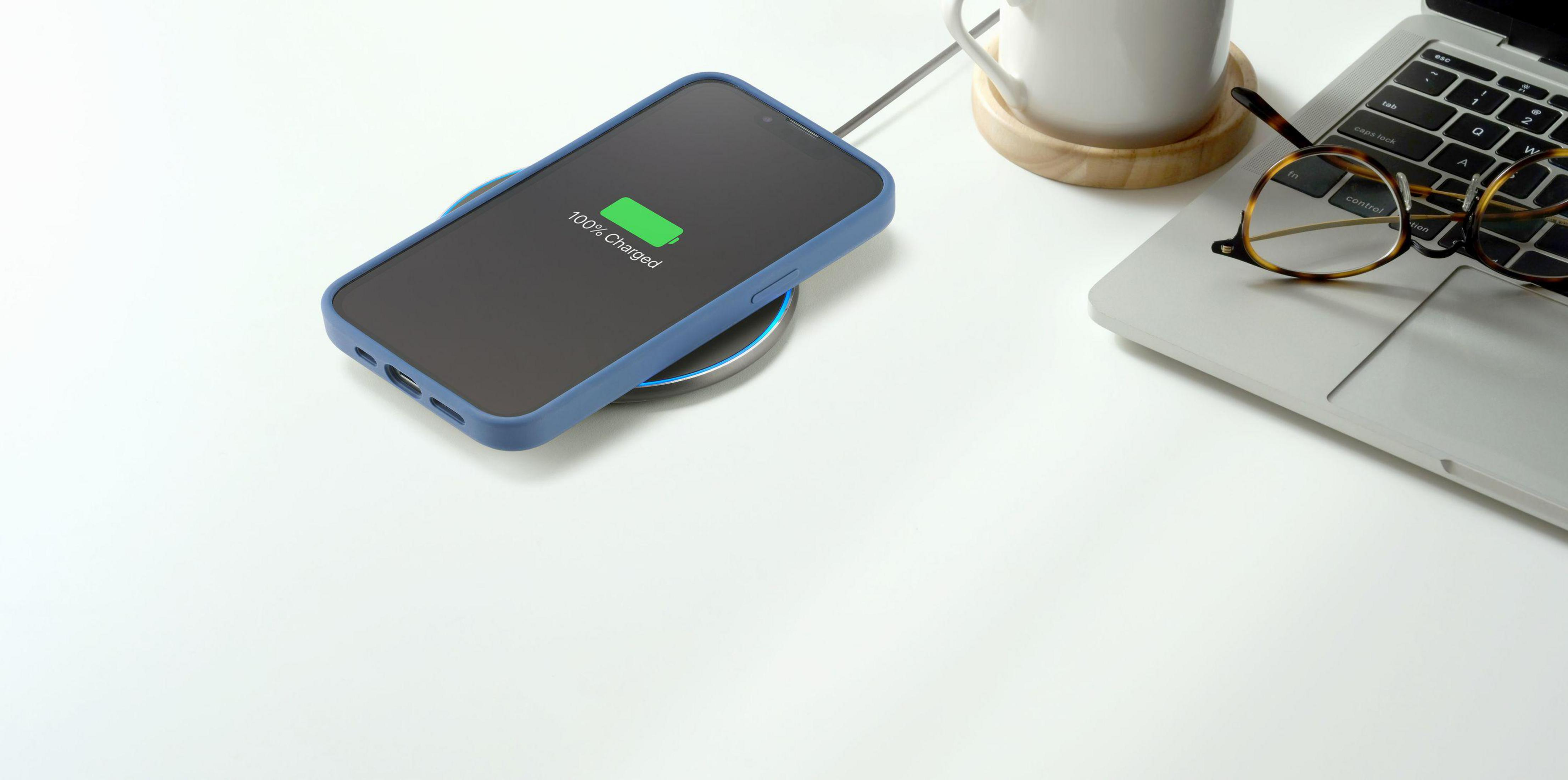 Telefon wird auf einem kabellosen Ladegerät aufgeladen. Das Telefon hat eine blaue Hülle und zeigt '100% geladen'.