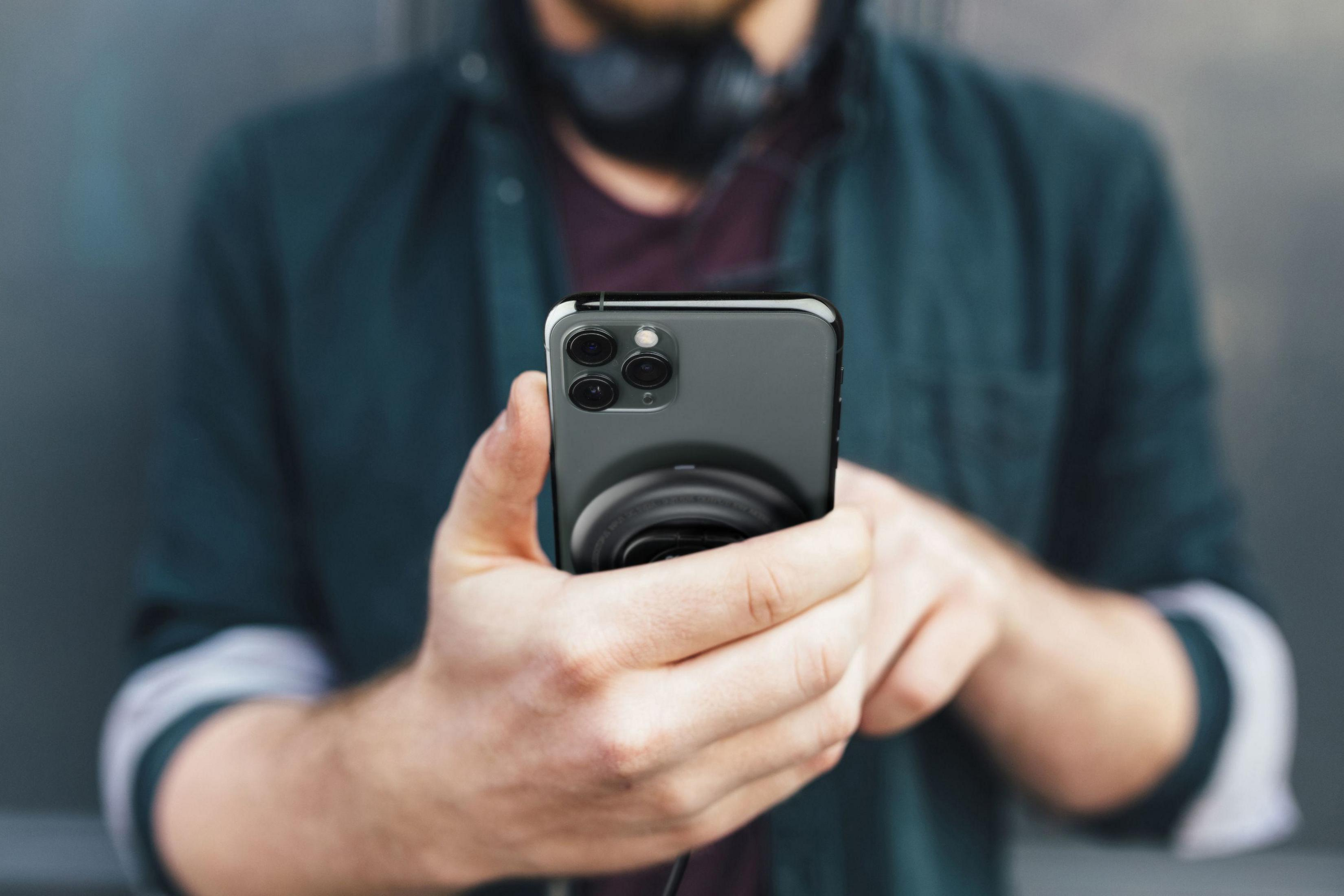 Una persona che tiene in mano uno smartphone nero con un pop socket nero.