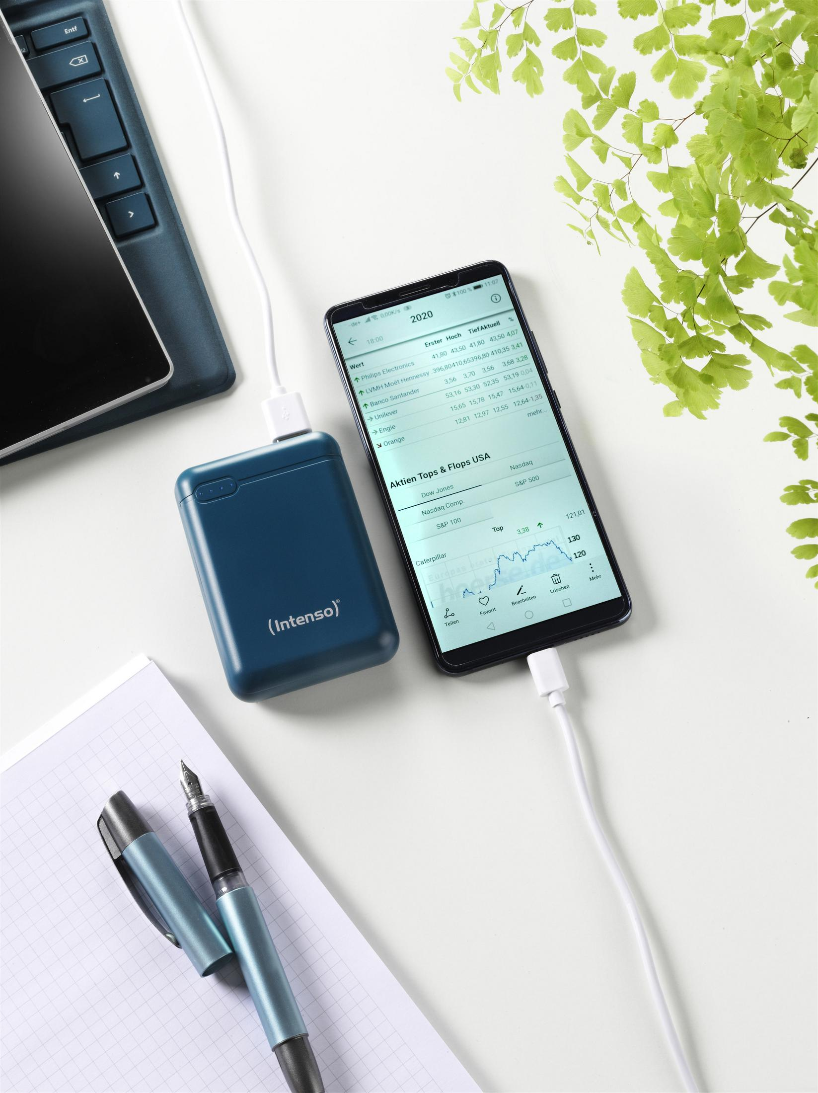 Un smartphone conectado a un cargador portátil, con bolígrafo y bloc de notas.