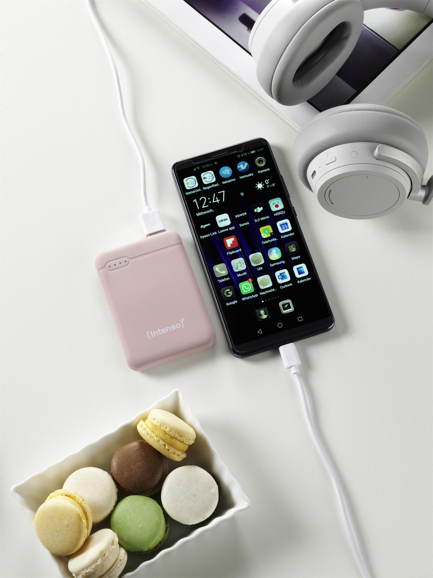 Telefon laden mit rosa Powerbank, Kopfhörern und Makronen auf Weiß.