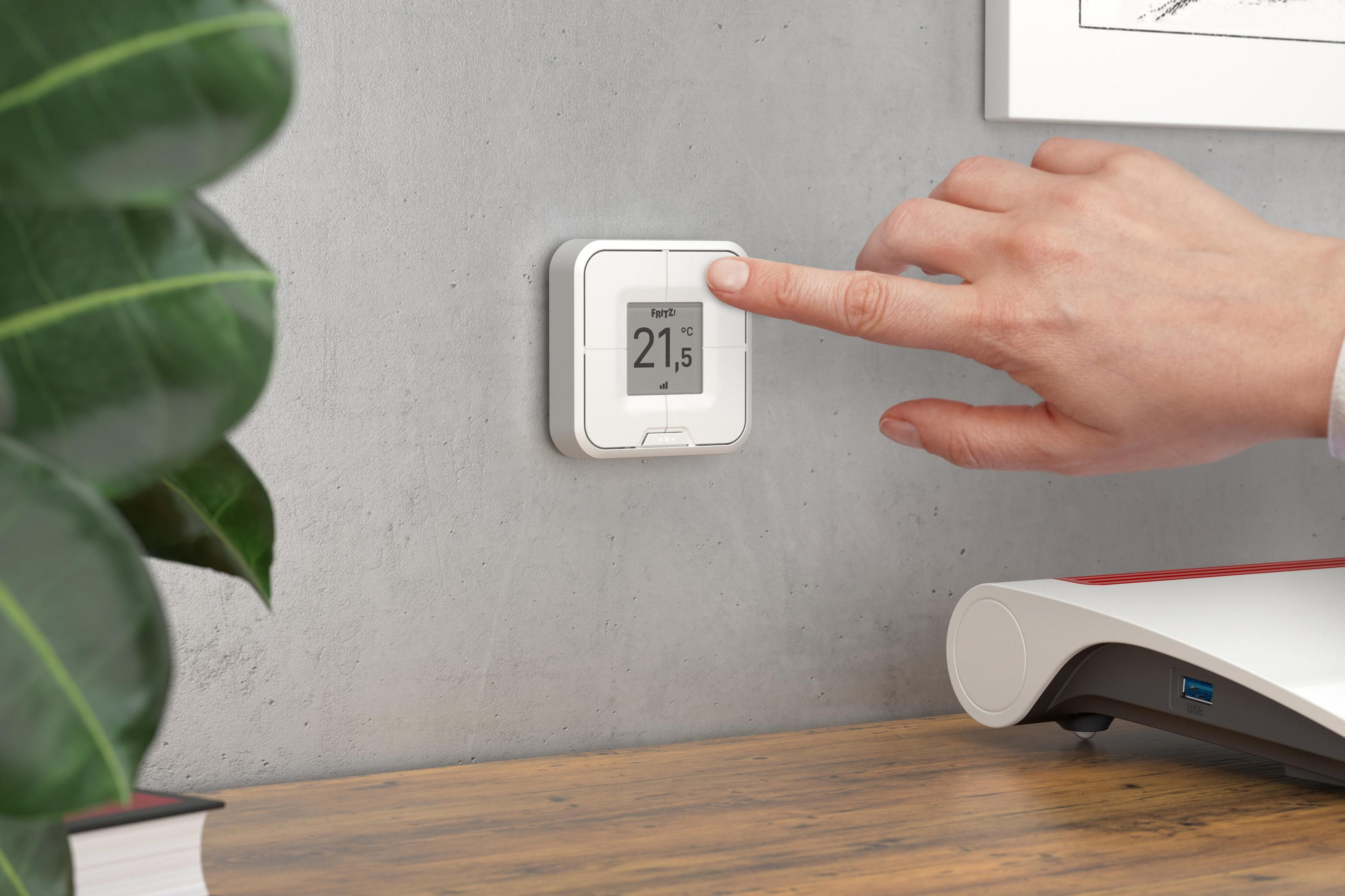 Eine Hand drückt auf einer weißen intelligenten Thermostat, der an einer grauen Wand montiert ist.