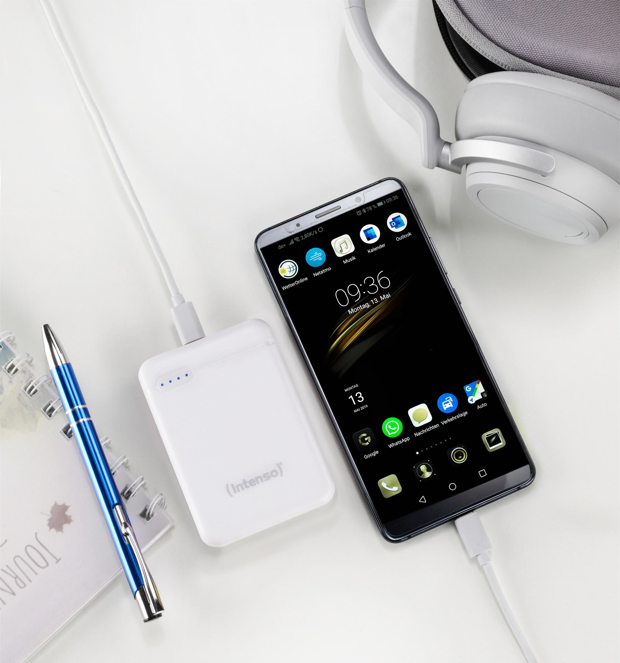 Een smartphone die oplaadt met een powerbank, pen en notitieboek op een wit oppervlak.