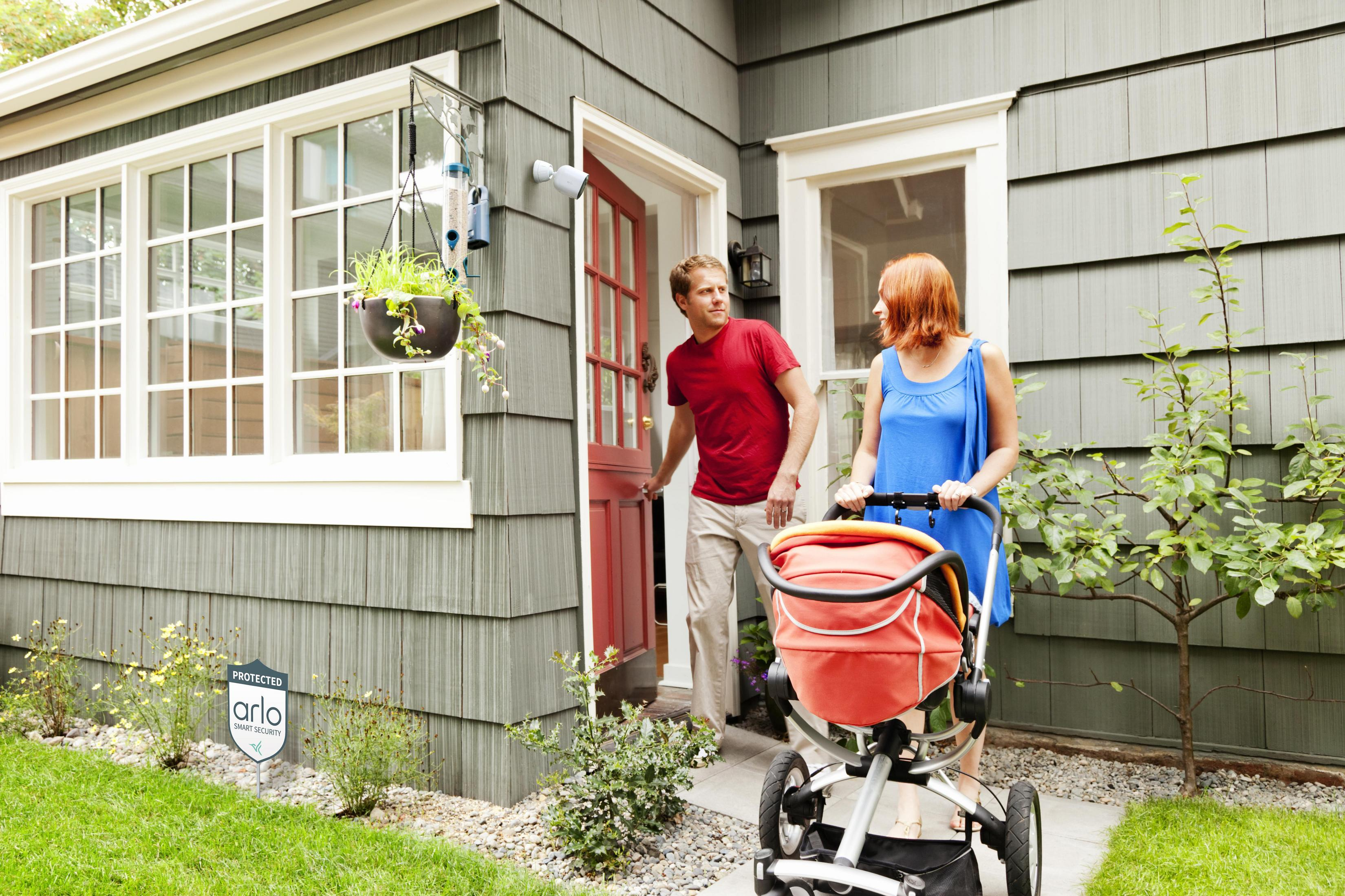 Para wchodząca do domu z czerwonymi drzwiami. Kobieta pcha wózek, a mężczyzna otwiera drzwi.