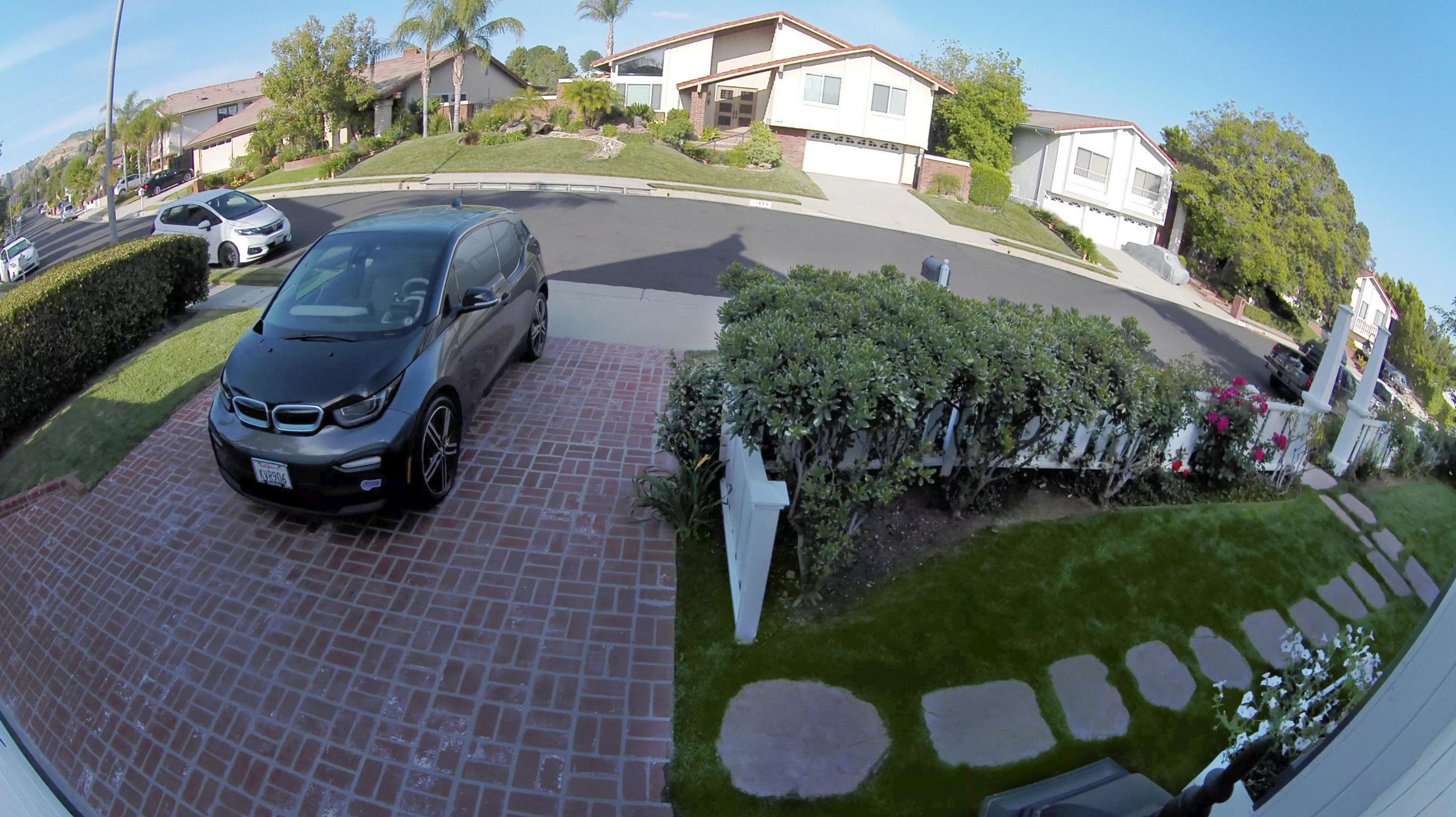 Widok ulicy z zaparkowanym samochodem przed domem. Zielona trawa i drzewa na pierwszym planie.