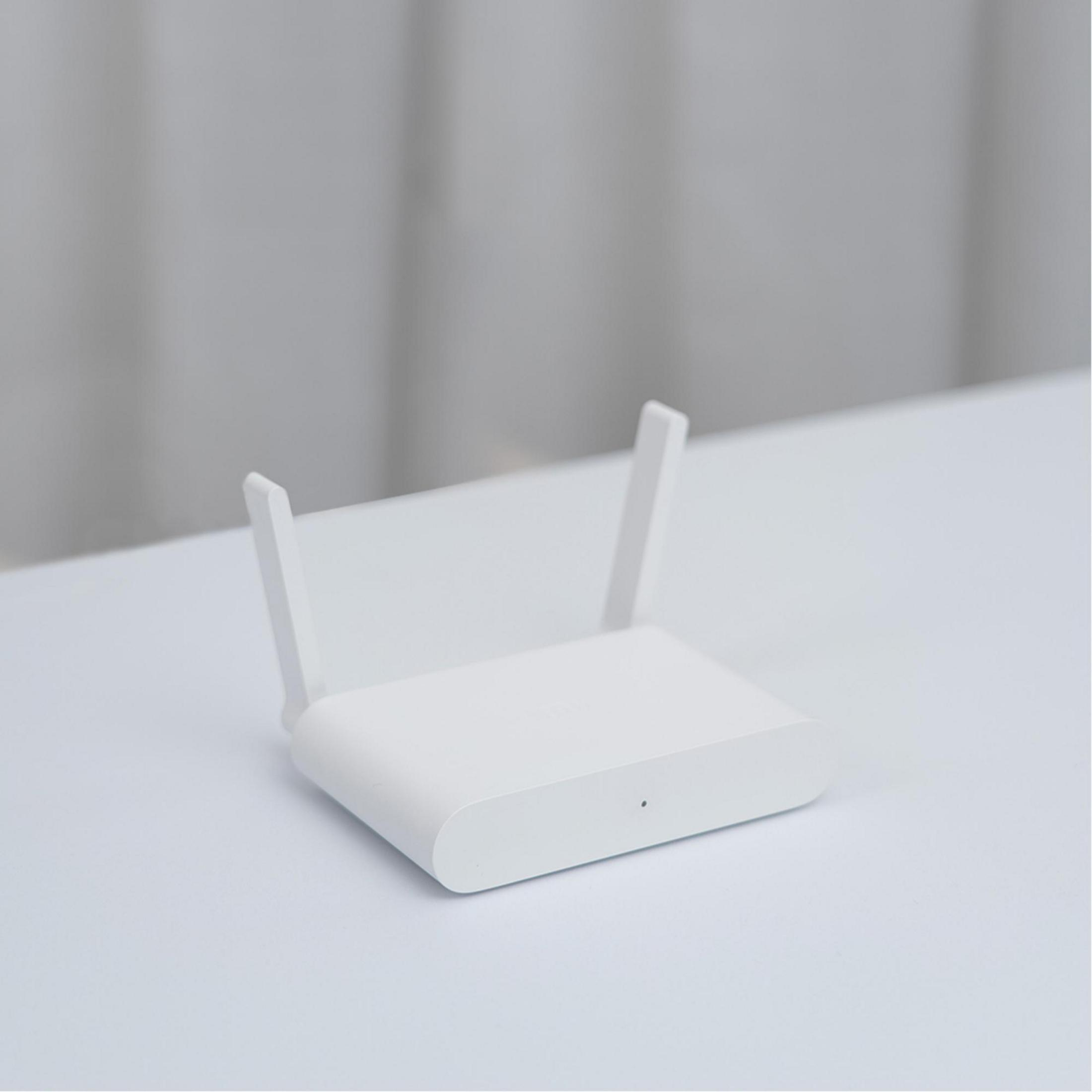 Un router bianco con due antenne su una superficie bianca. Lo sfondo è una tonalità neutra sfocata.