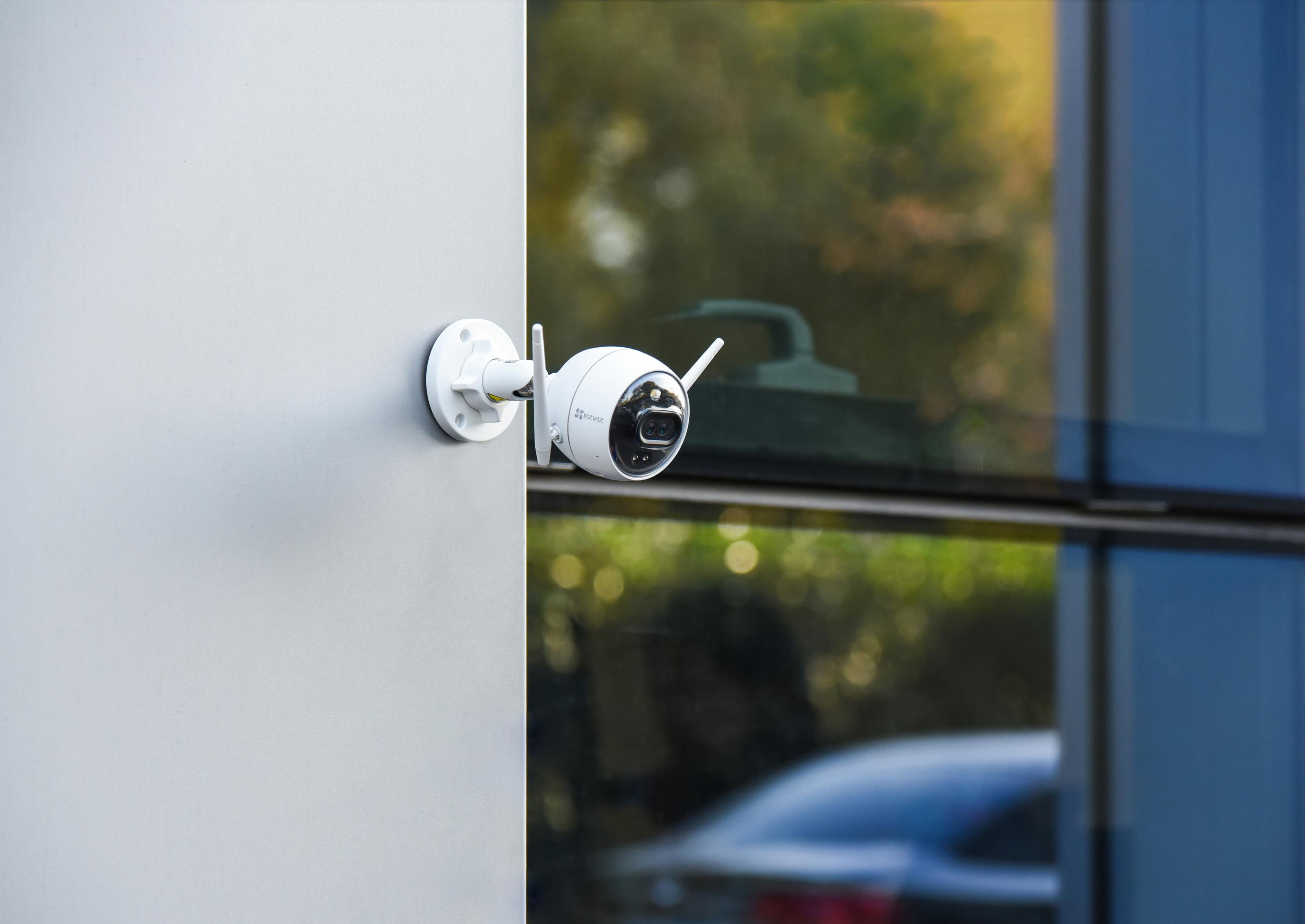 Telecamera di sicurezza bianca montata su un muro grigio accanto a un edificio di vetro.
