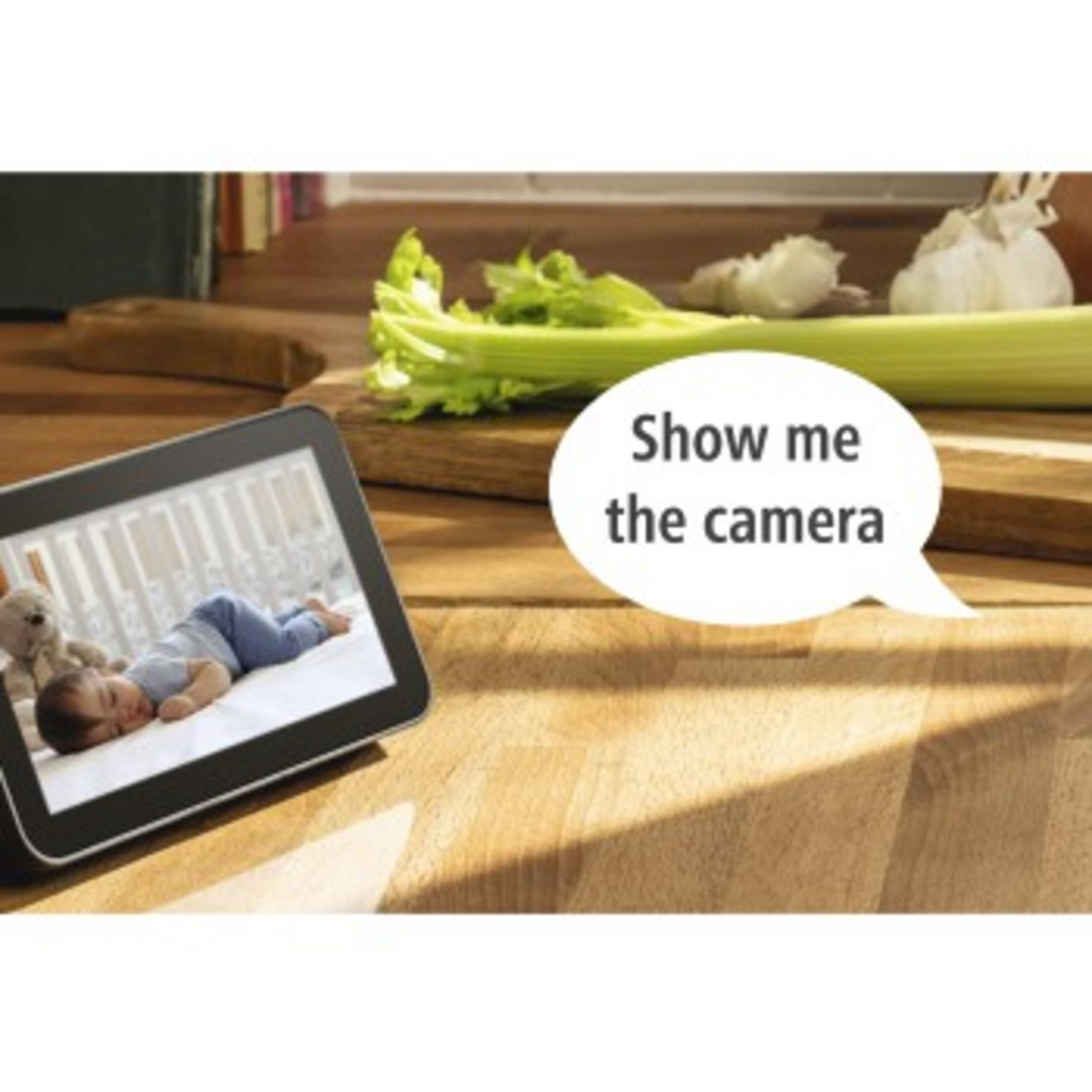 Tablet pokazuje śpiące dziecko. Warzywa leżą na drewnianej powierzchni. Dymek mówi: „Pokaż mi kamerę”.