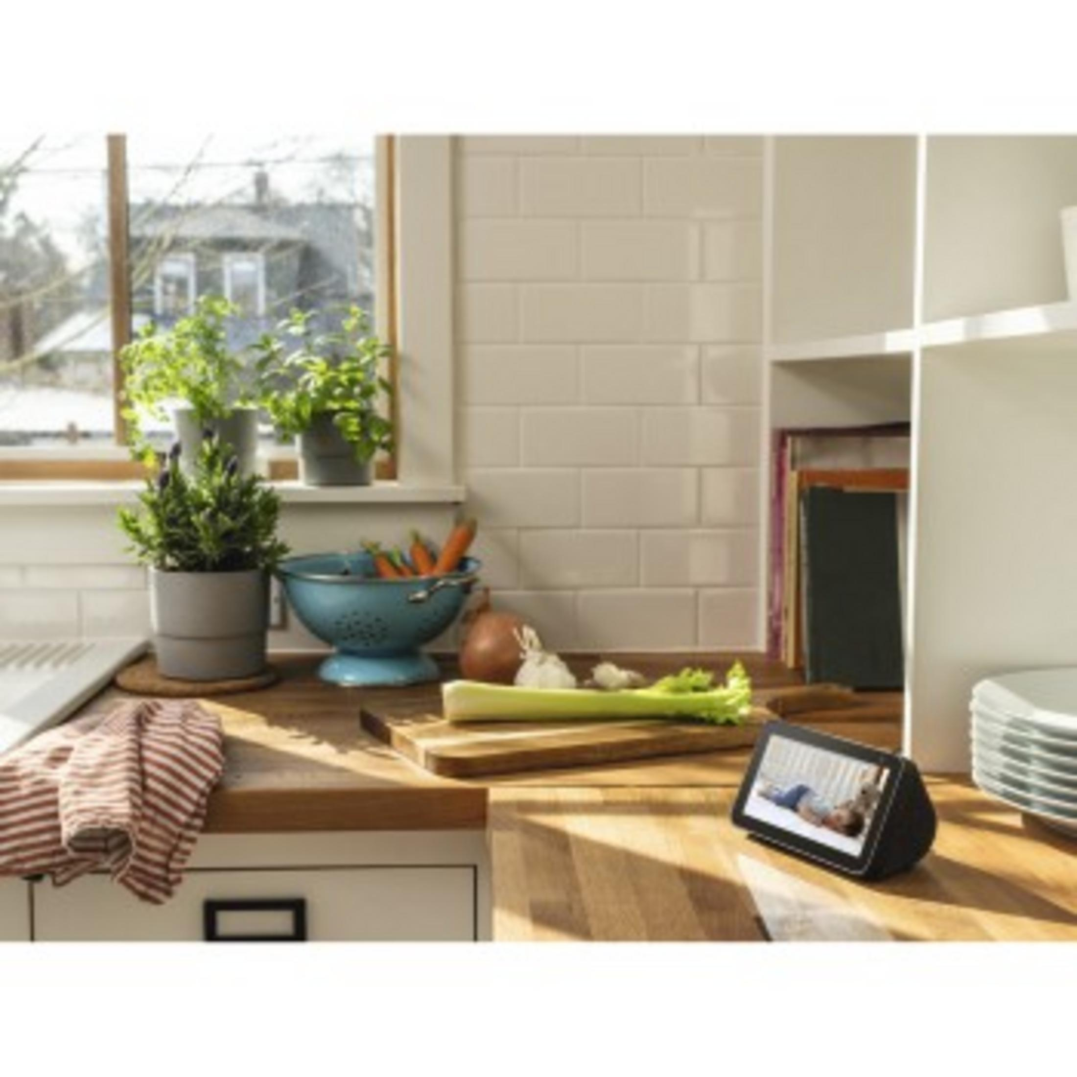 Inteligentny wyświetlacz na blacie kuchennym z roślinami i jedzeniem. Okno w tle.