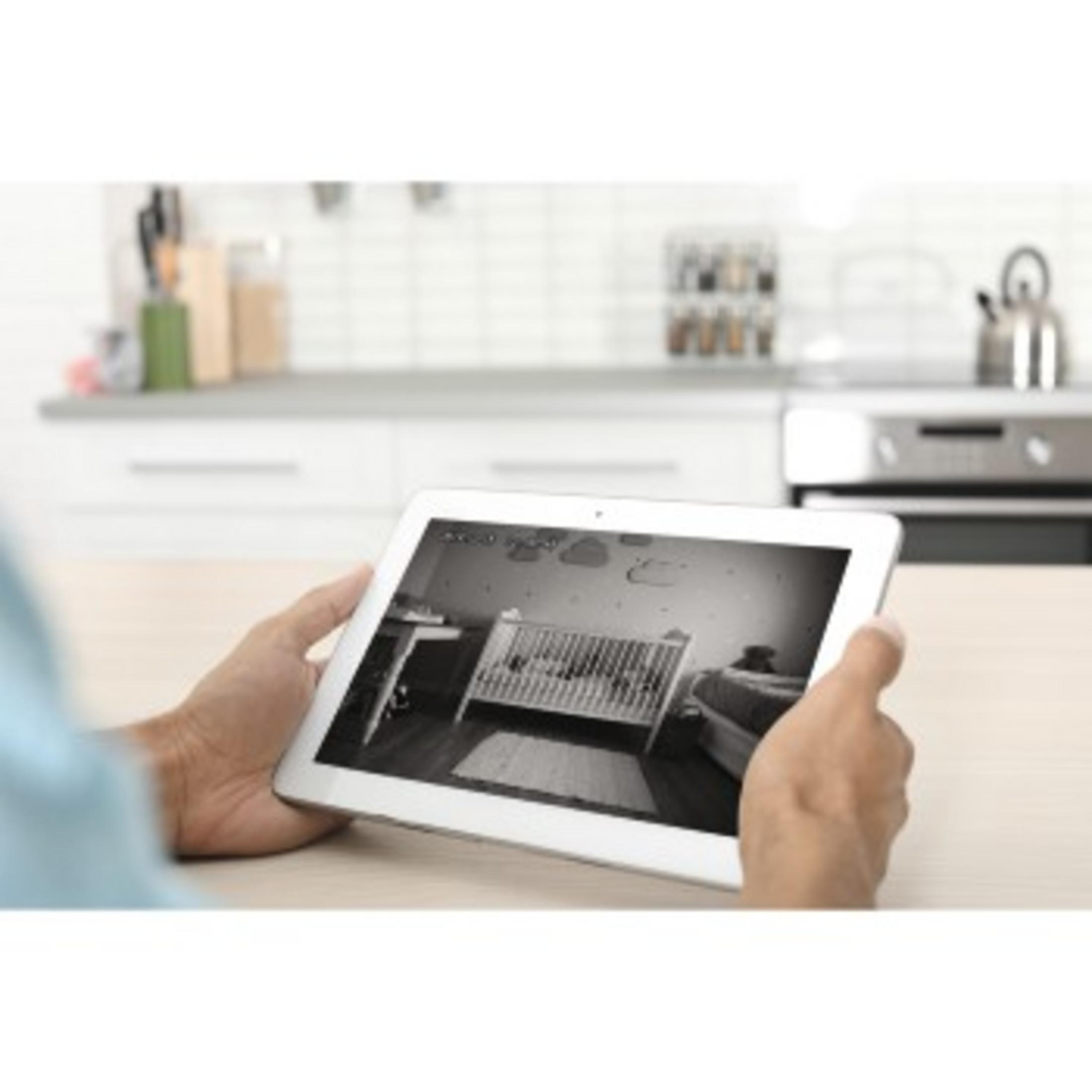 Osoba trzymająca tablet z widokiem na łóżeczko i pokój dziecka, widoczne z kamery bezpieczeństwa.