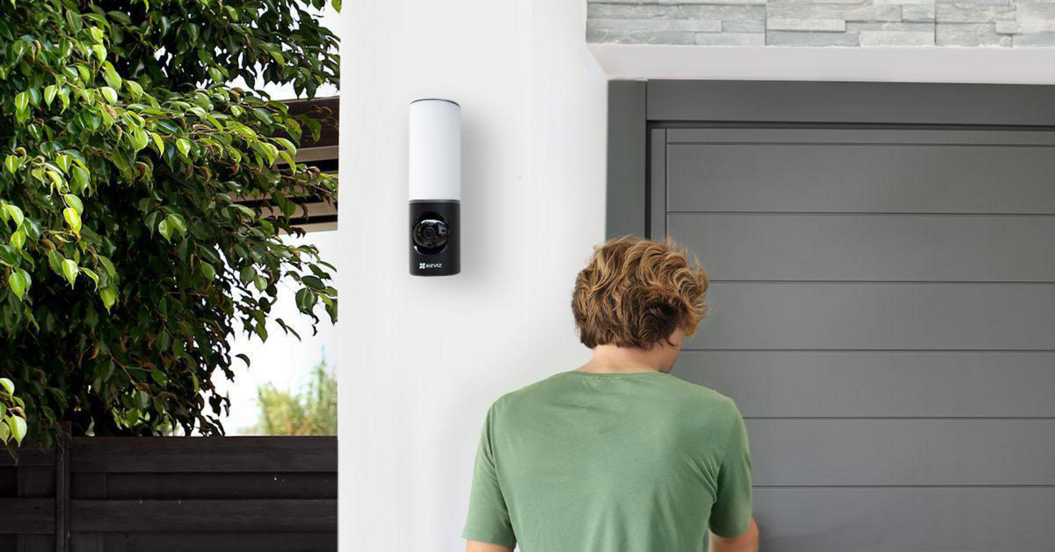 Kamera bezpieczeństwa zamontowana na białej ścianie obok drzwi. Mężczyzna zbliża się do drzwi.