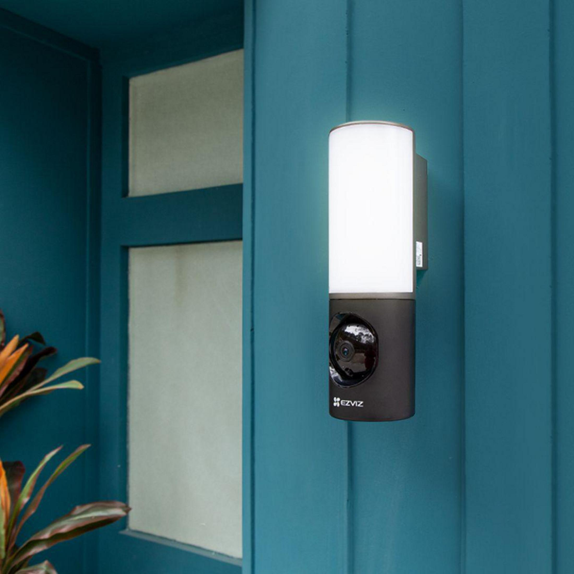 Zewnętrzna lampa ścienna i kamera bezpieczeństwa zamontowane na niebieskiej ścianie.