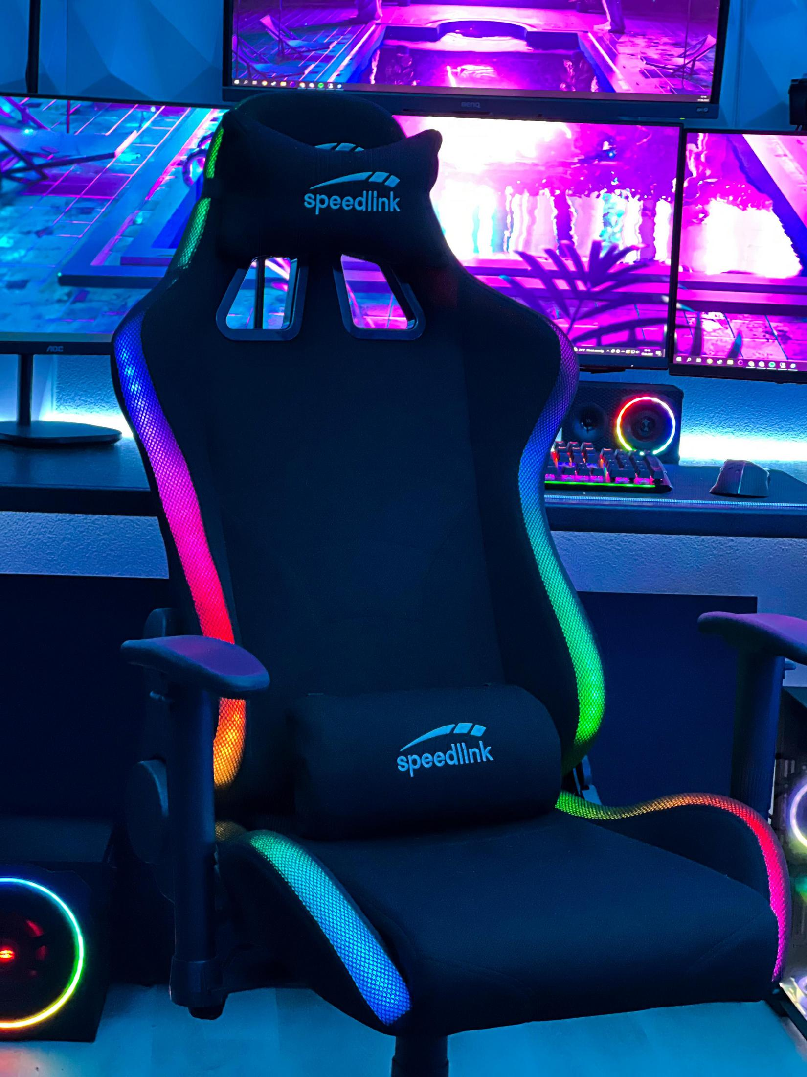 Silla gaming con luces LED de colores. Con logotipo de Speedlink. Los monitores son visibles en el fondo.
