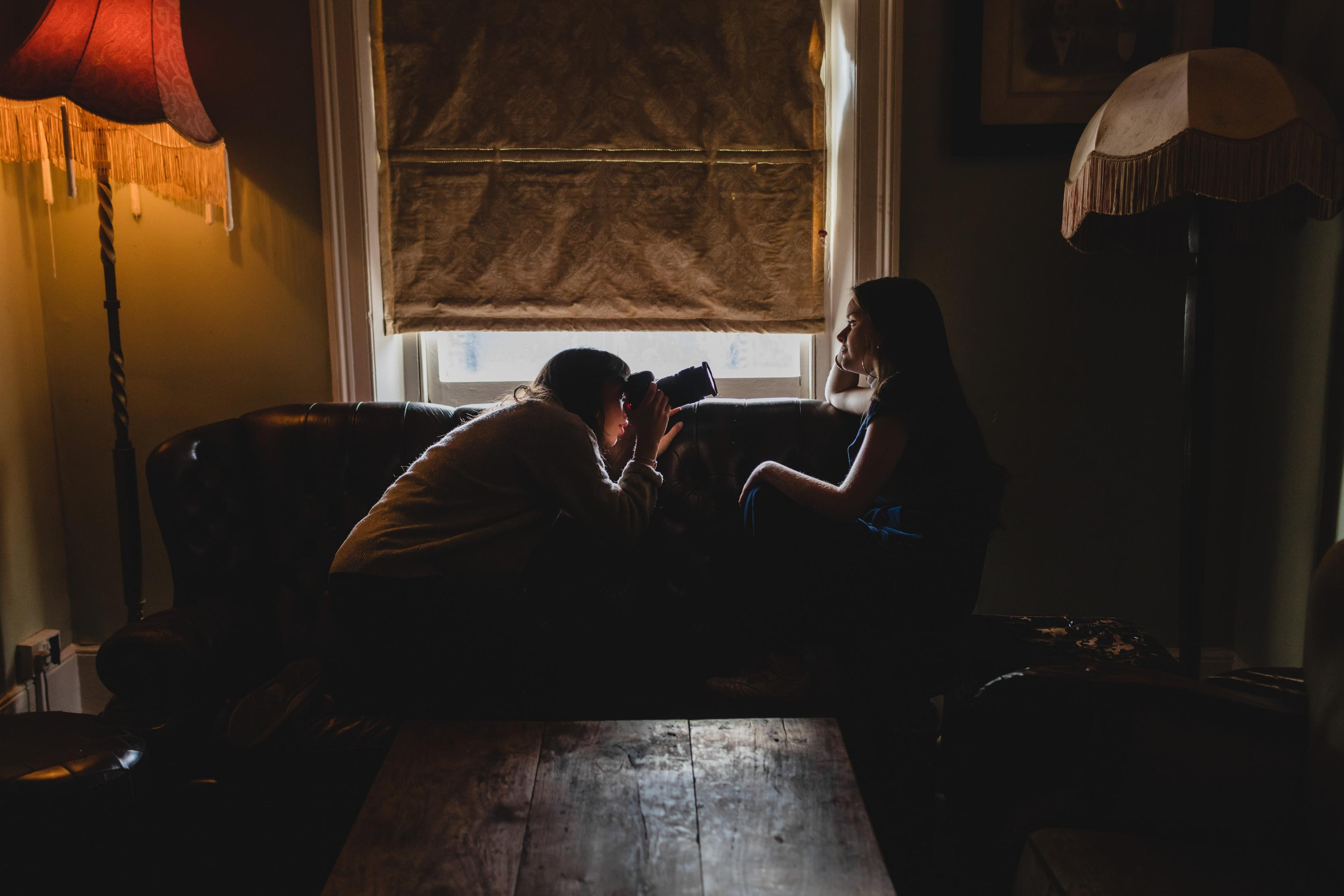 Zwei Frauen in einem schwach beleuchteten Raum, eine macht Fotos mit einer Kamera, die andere schaut zu.