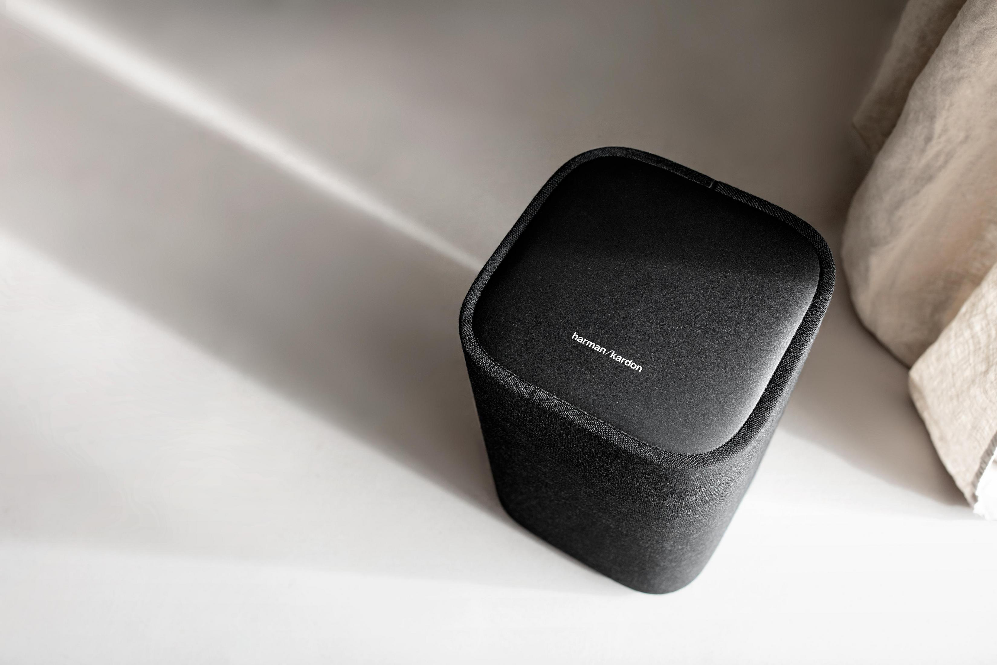 Een zwarte Harman/Kardon-luidspreker op een wit oppervlak met een linnen doek.