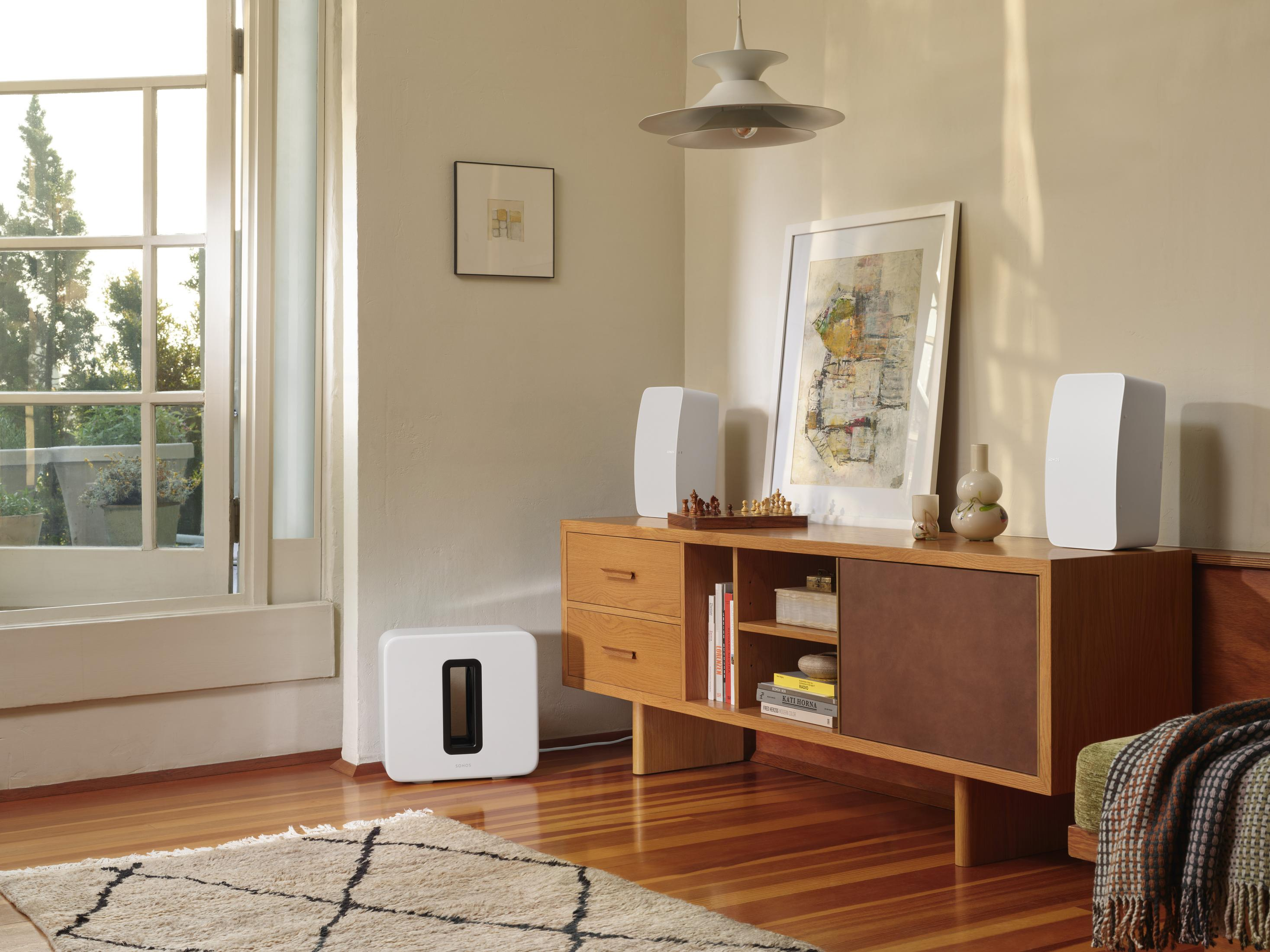 Pokój z drewnianą szafką, głośnikami i subwooferem. Obraz wisi nad szafką.