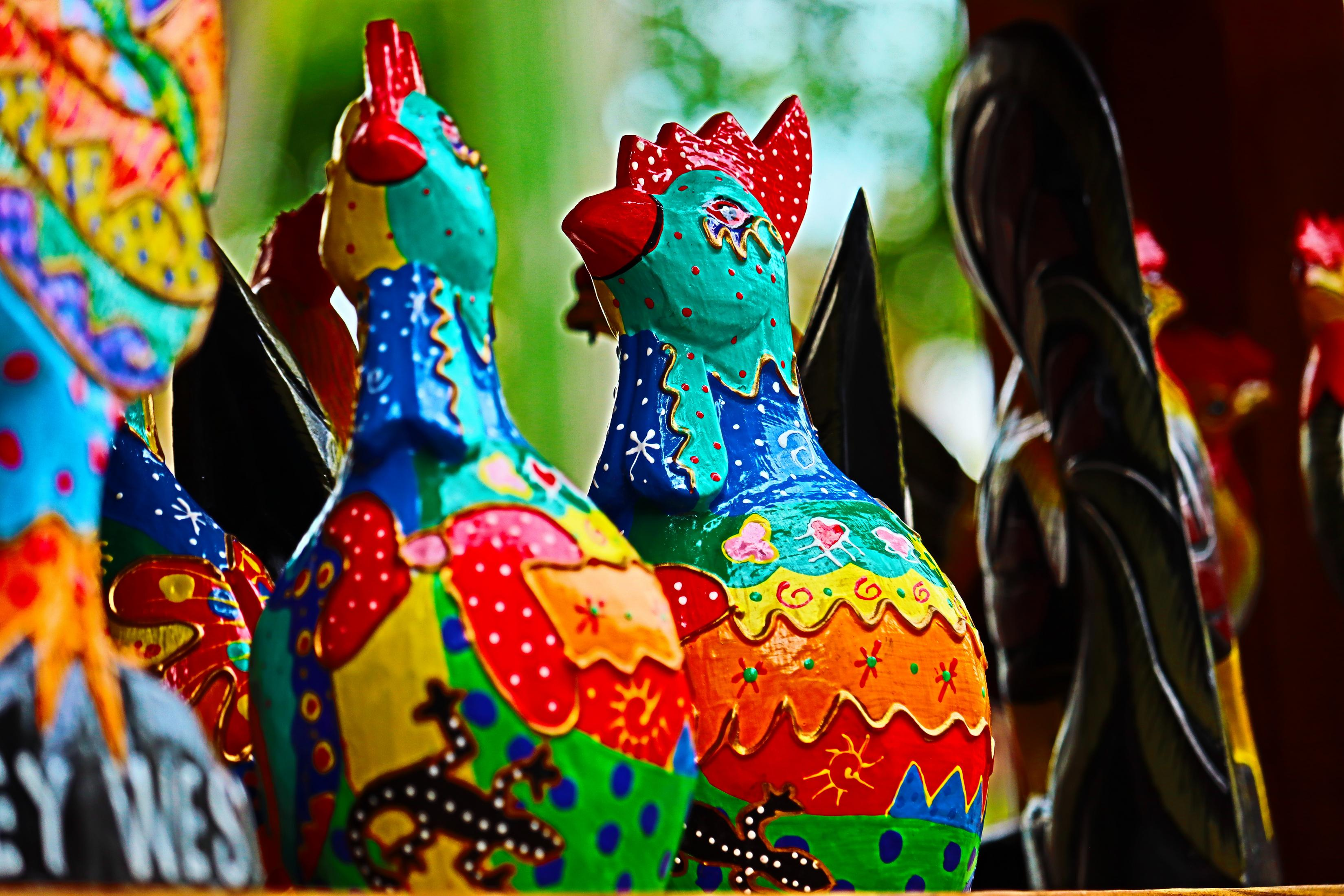 Ręcznie malowane drewniane posągi kogutów. Jasne kolory ze skomplikowanymi wzorami. Rozmyte tło.