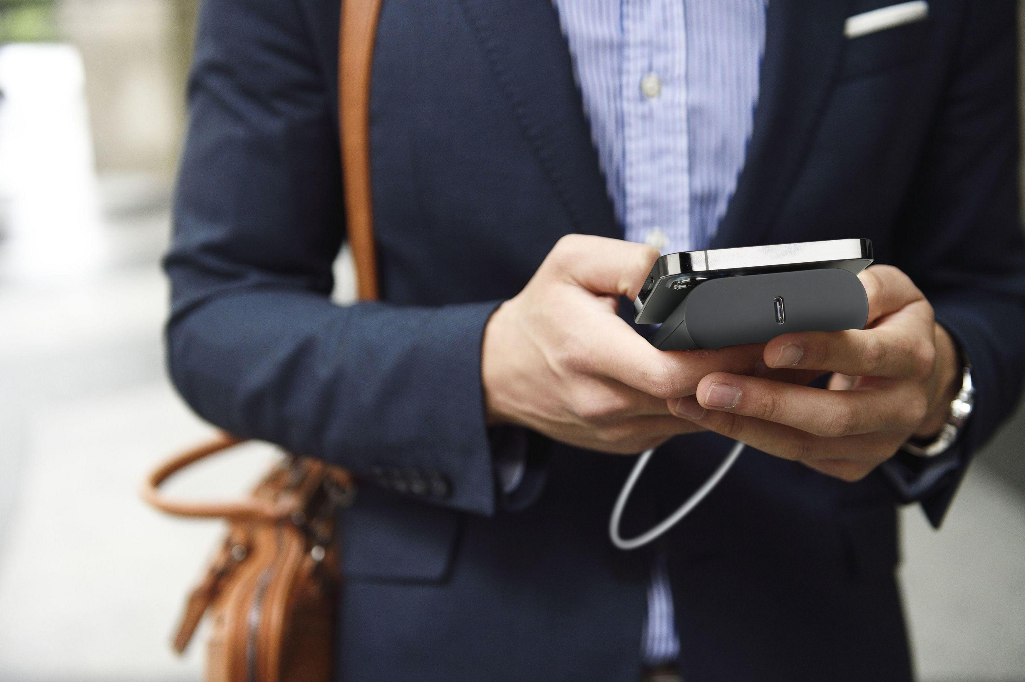Ein Mann im Anzug hält ein Ladegerät mit einem Telefon. Eine Ledertasche ist auf seiner Schulter.