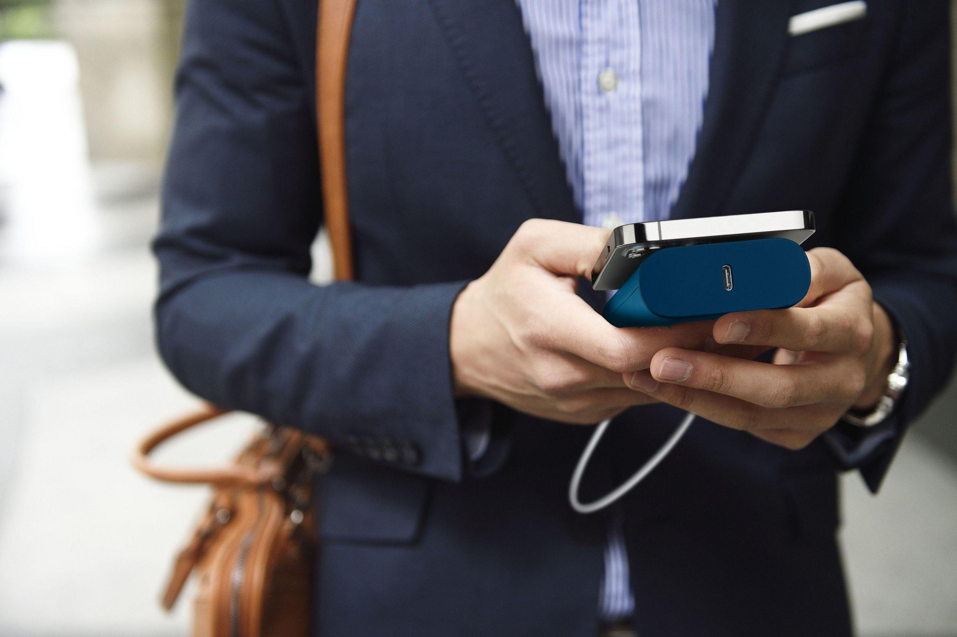 Mann hält Telefon und tragbares Ladegerät, beide blau, in der Nähe einer Tasche.