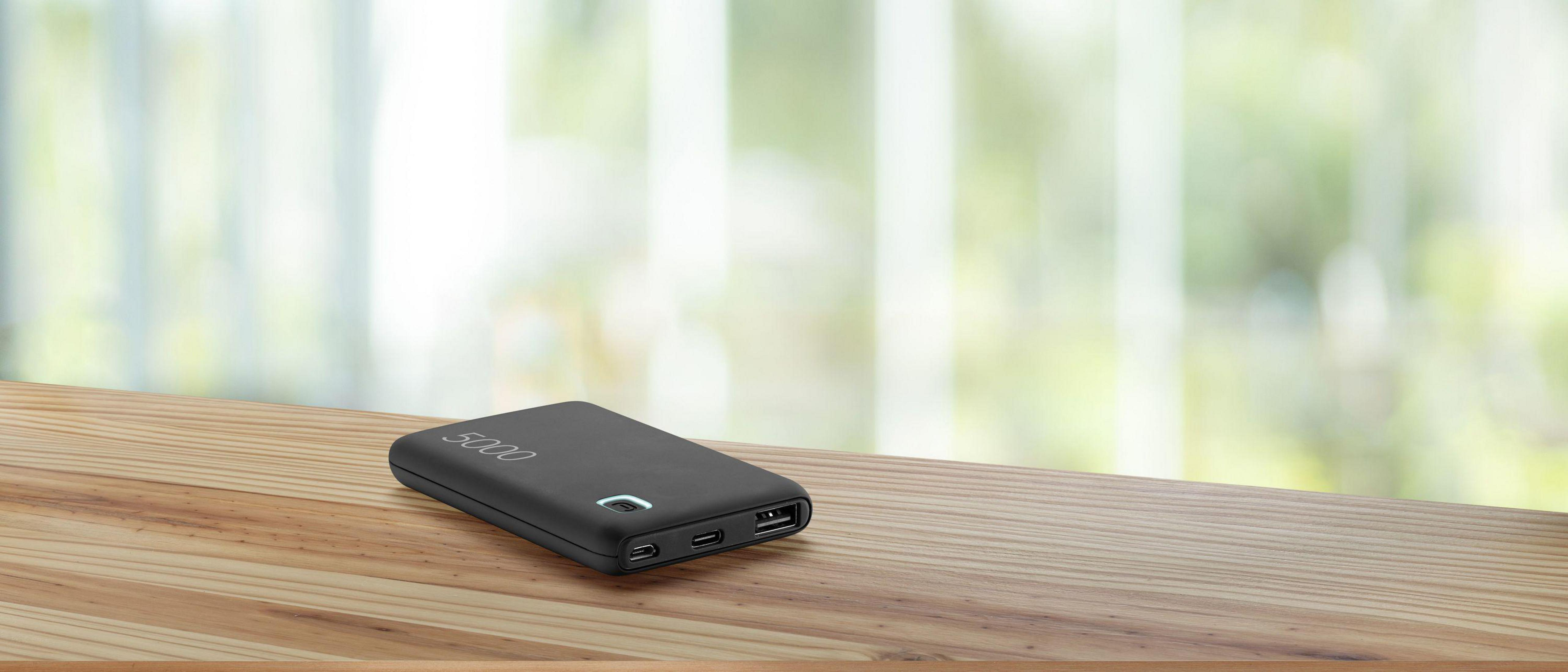 Schwarze Powerbank auf einem Holztisch. Die Powerbank hat die Zahl 5000 darauf.