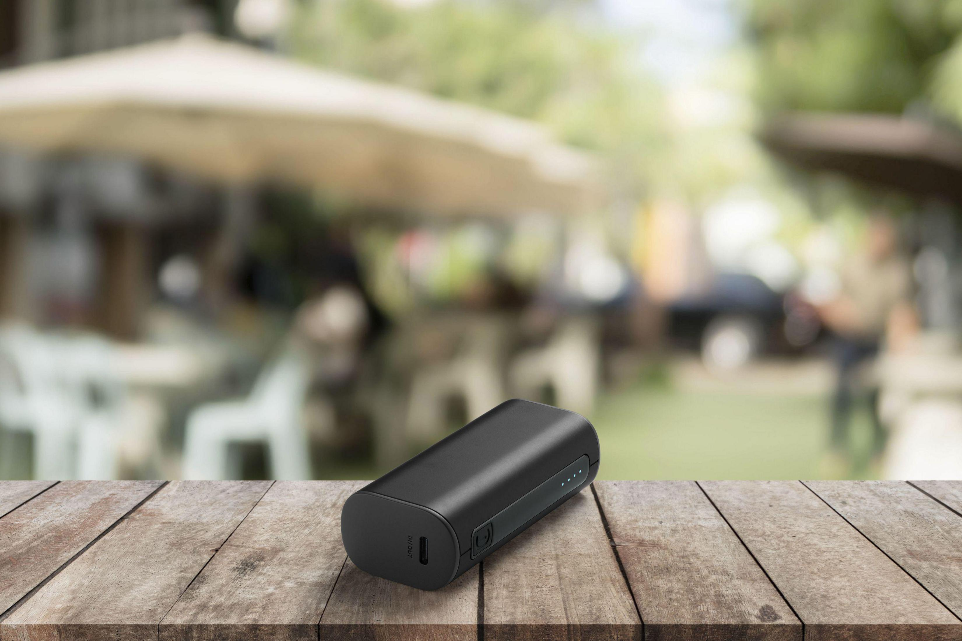 Eine schwarze Powerbank auf einem Holztisch, mit verschwommenem Hintergrund im Freien.