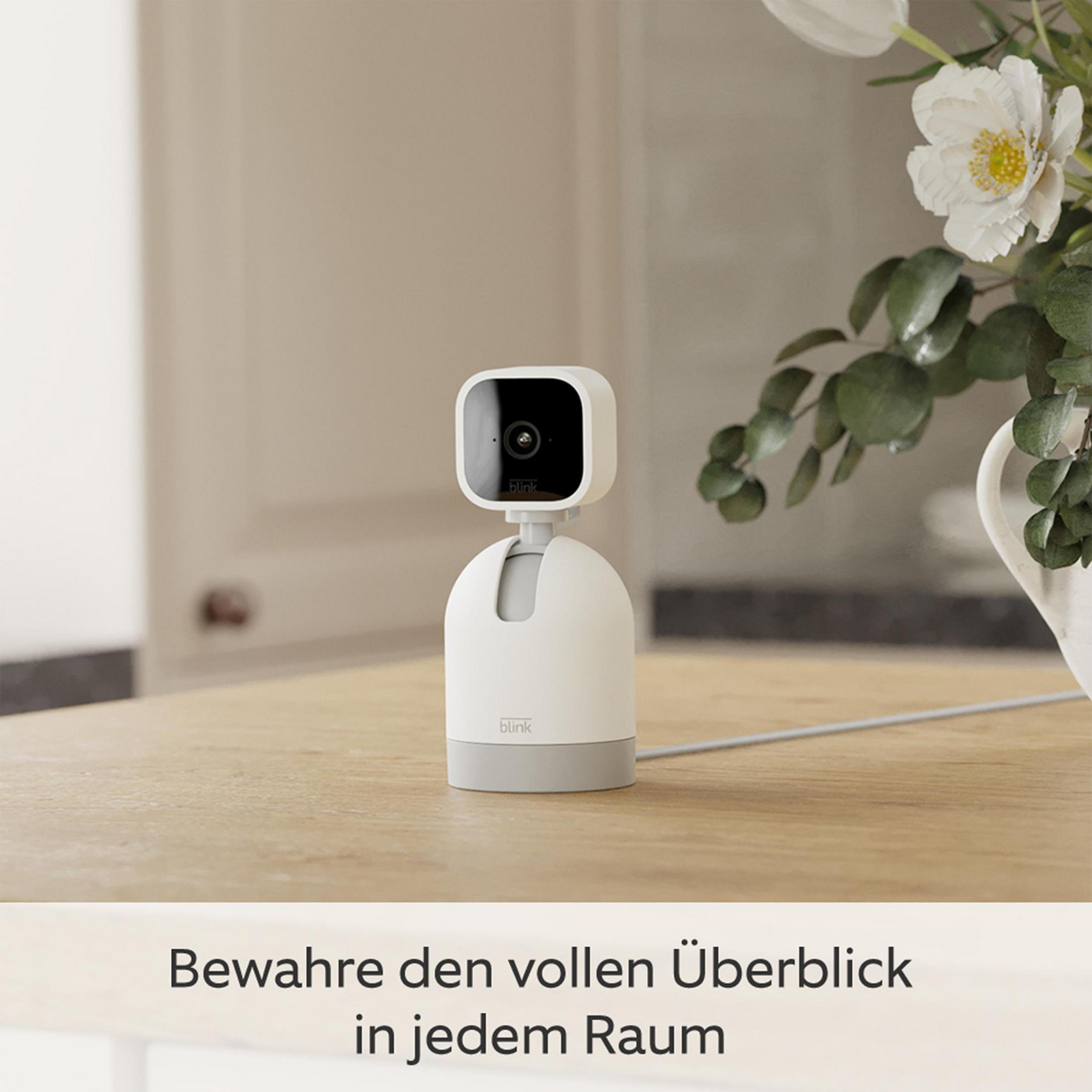 Biała i szara kamera bezpieczeństwa domowego na drewnianym stole, z tekstem poniżej.
