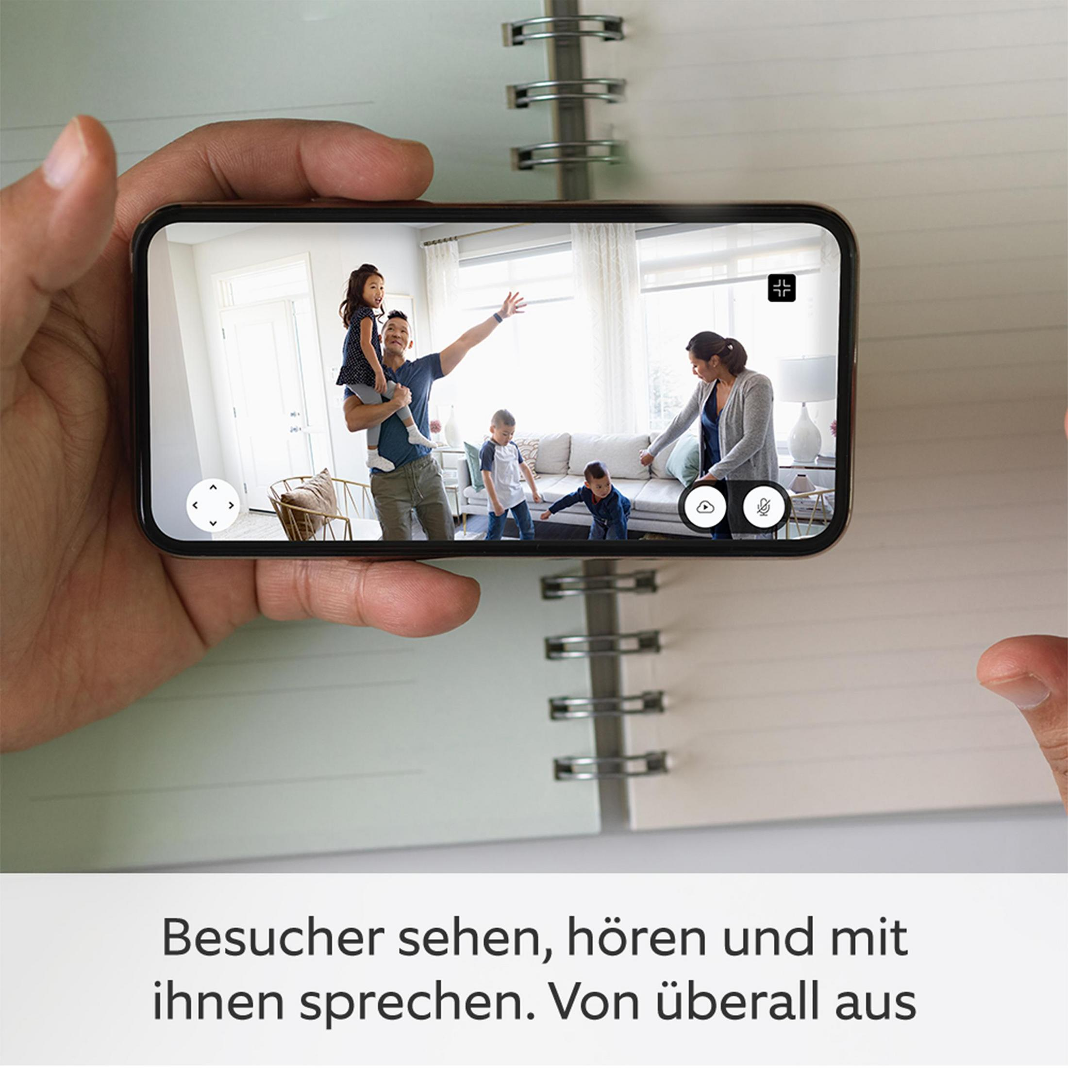 Osoba trzymająca telefon pokazujący rodzinę w salonie, z otwartym notatnikiem.