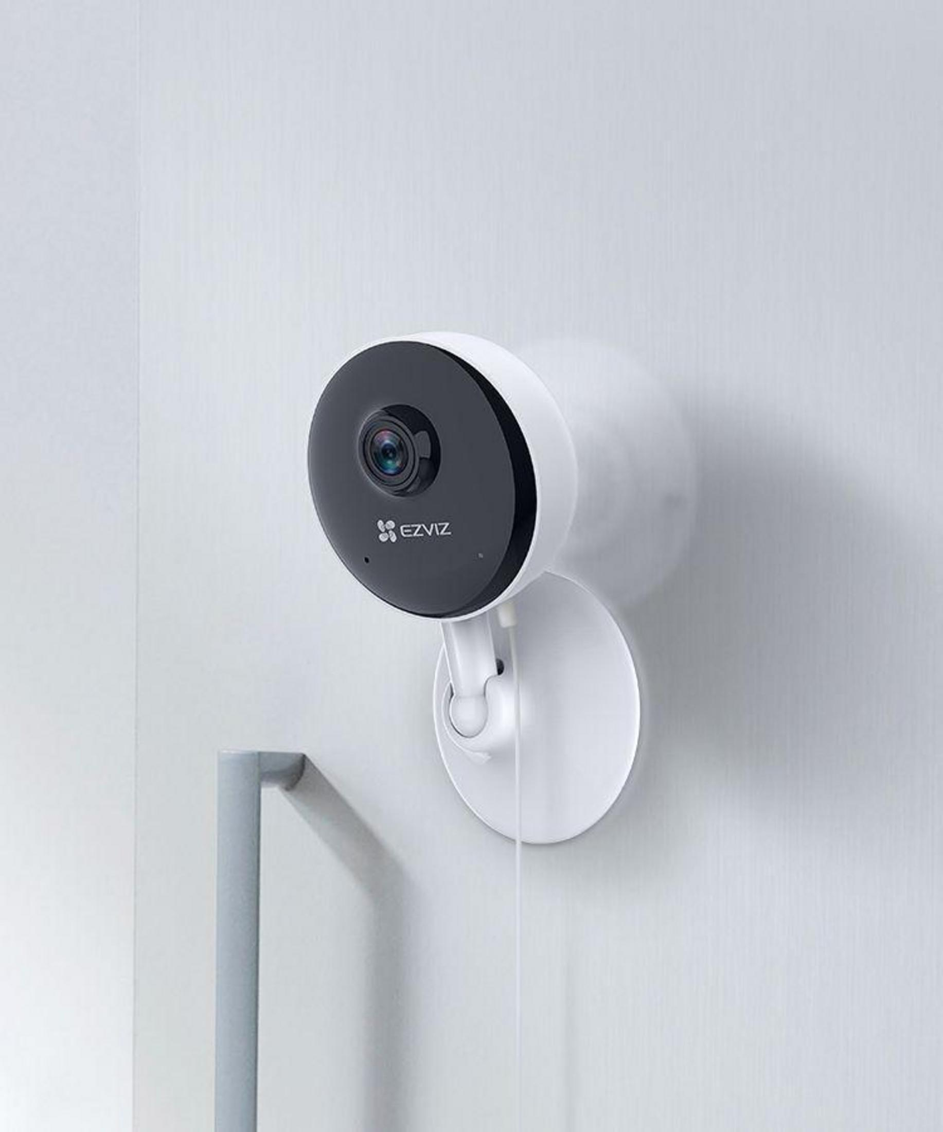 Biała i czarna kamera bezpieczeństwa zamontowana na białej ścianie. Kamera ma czarny obiektyw i białą podstawę.