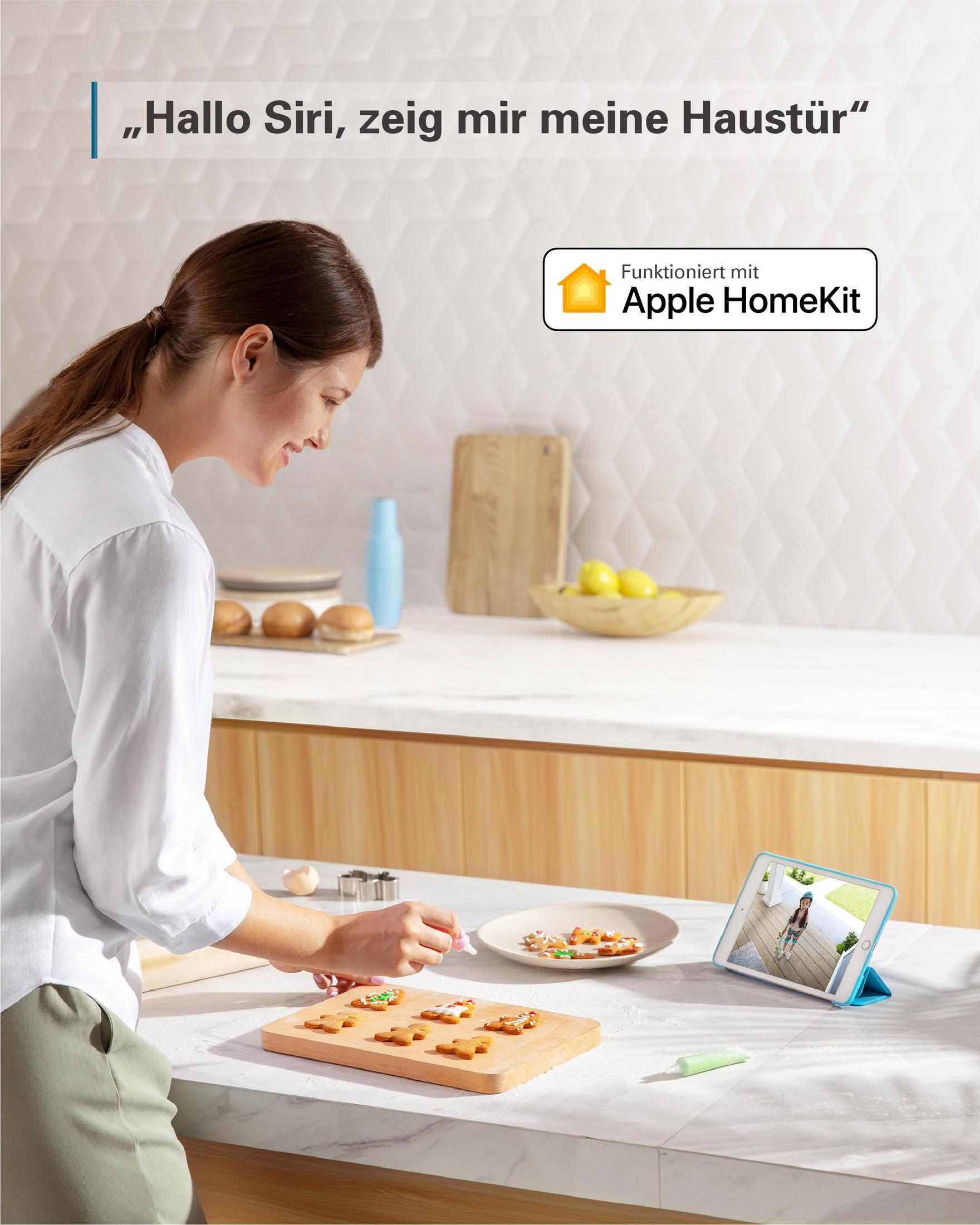 Frau dekoriert Lebkuchen, während sie die Türkamera auf einem Tablet betrachtet.