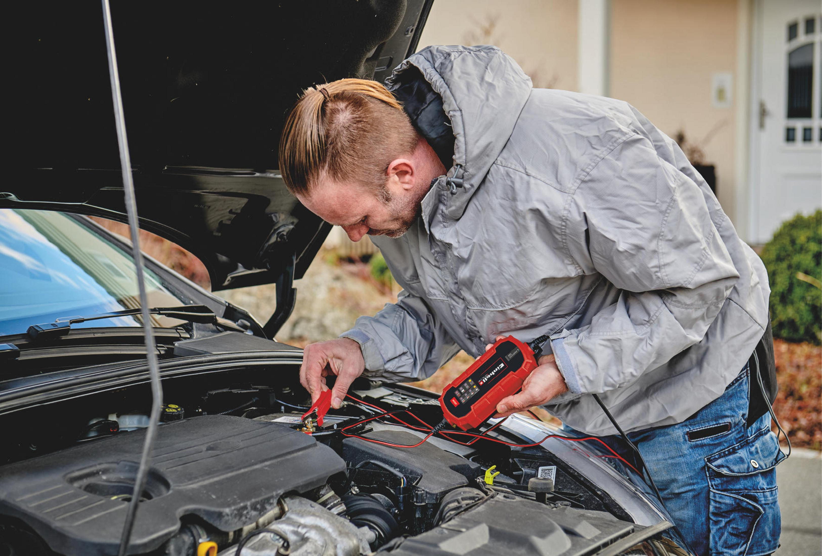 Mann arbeitet an einem Auto. Er hält ein rotes Gerät und verbindet die Drähte.